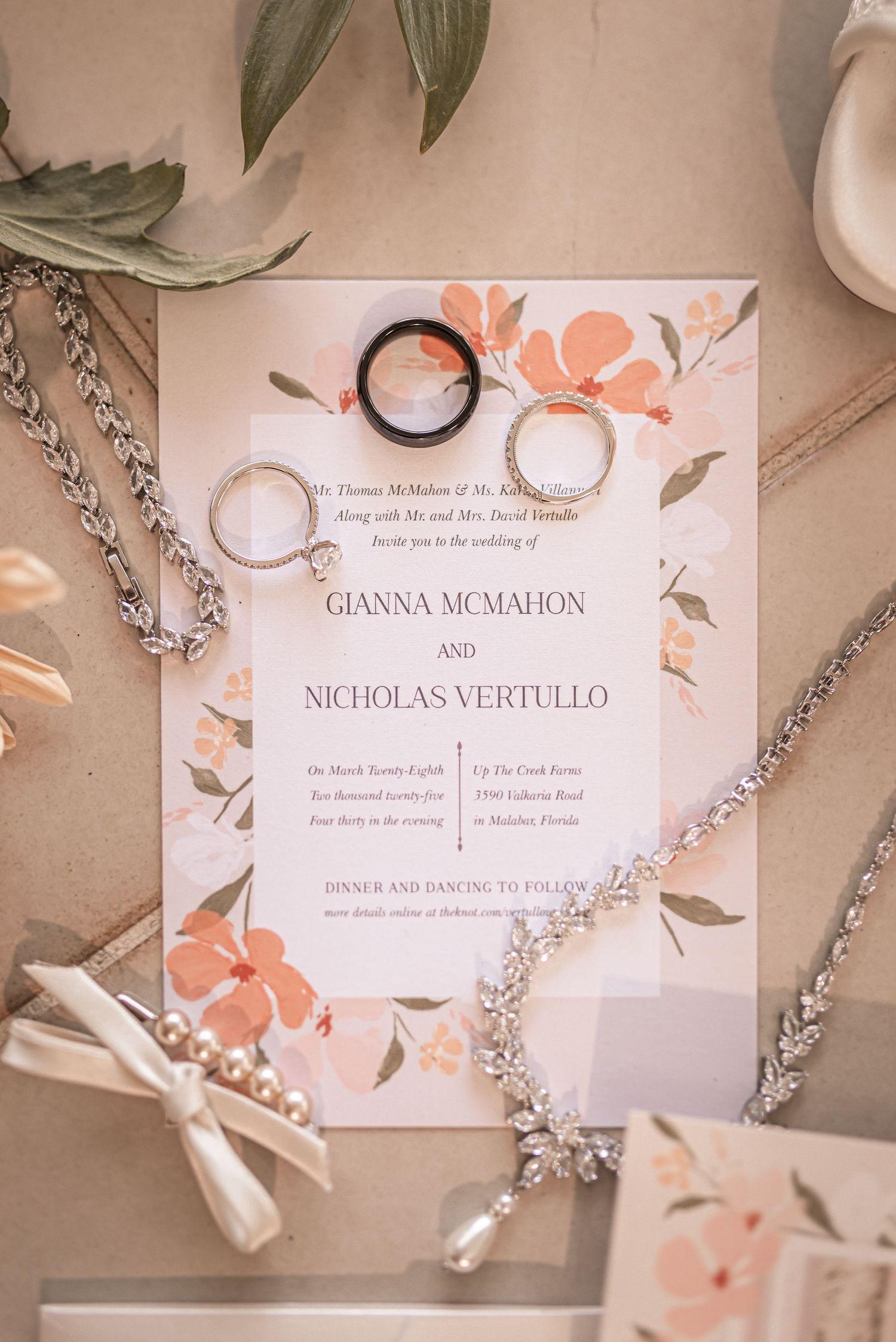 Wedding invitation with floral design in peach tones displayed with wedding rings and jewelry accessories.