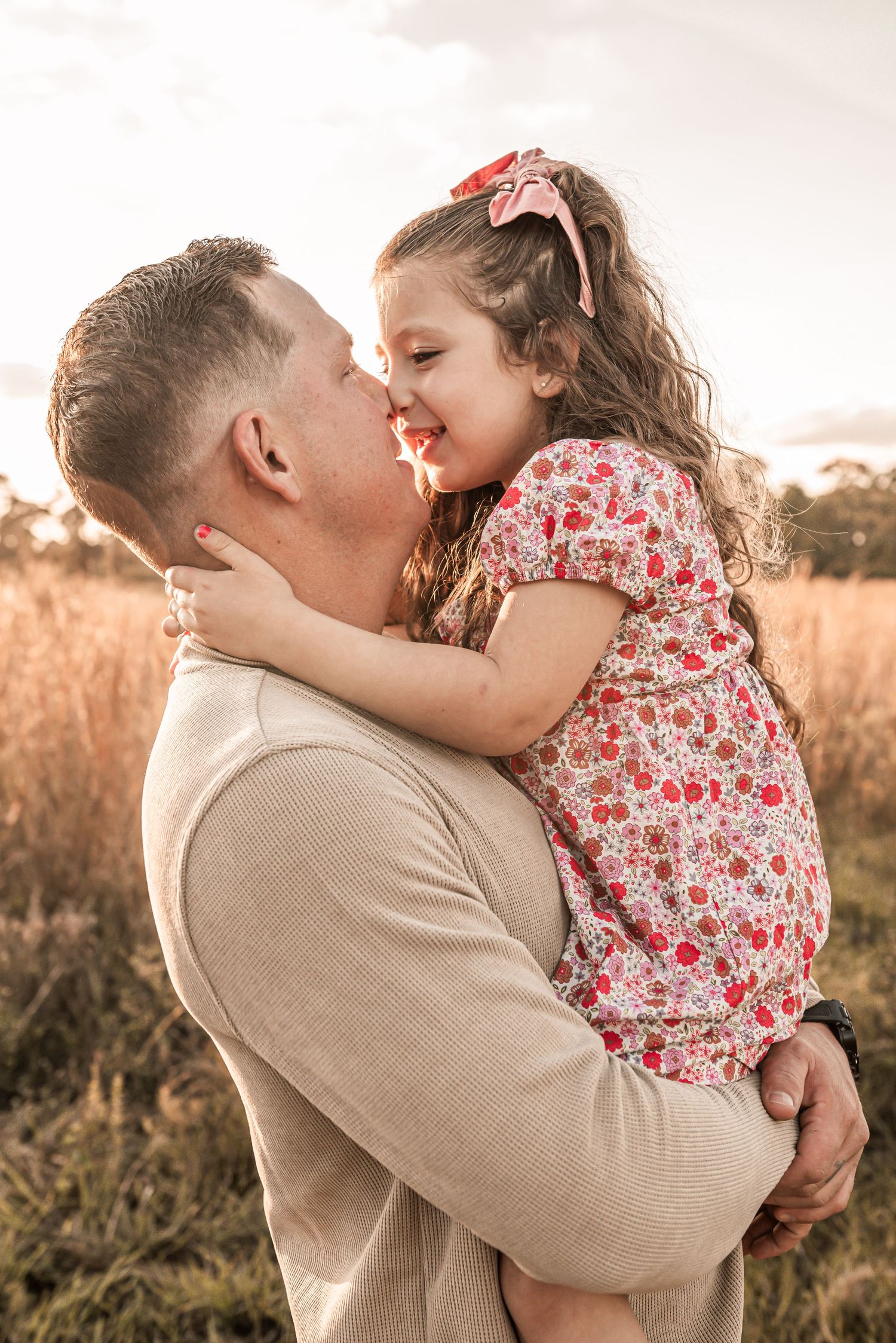Sweet candid moment between parent and child in floral dress embracing at sunset in golden field.