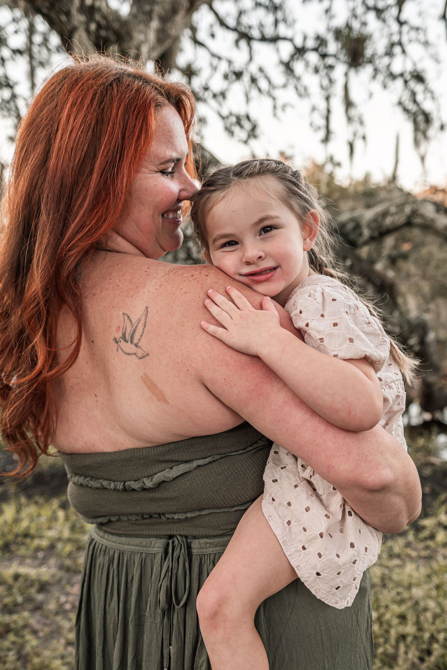 A tender moment outdoors as a woman in a green dress embraces a young girl in a polka dot dress against a nature backdrop.