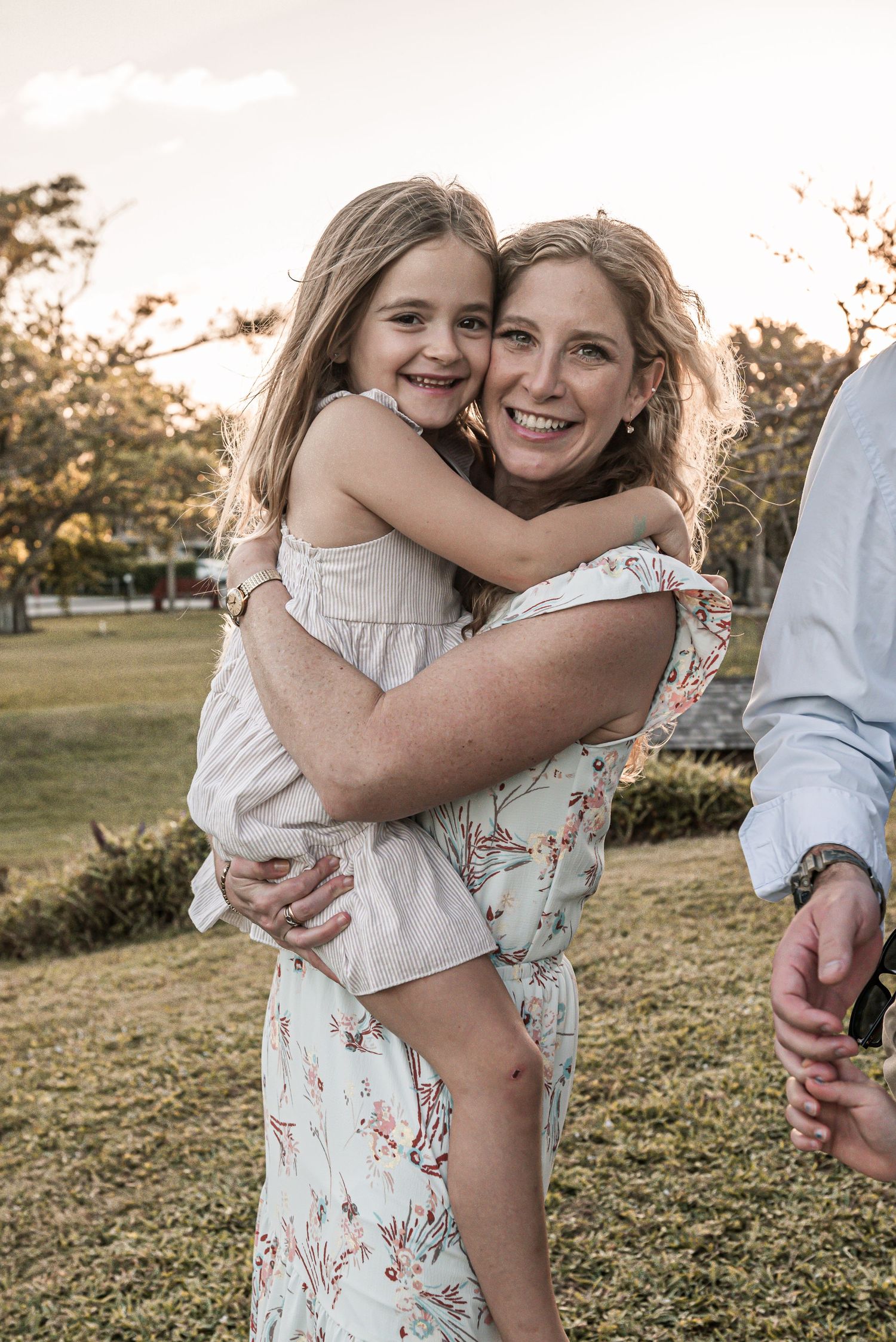 A heartwarming outdoor moment shared between a parent and child hugging while wearing light-colored dresses at sunset.