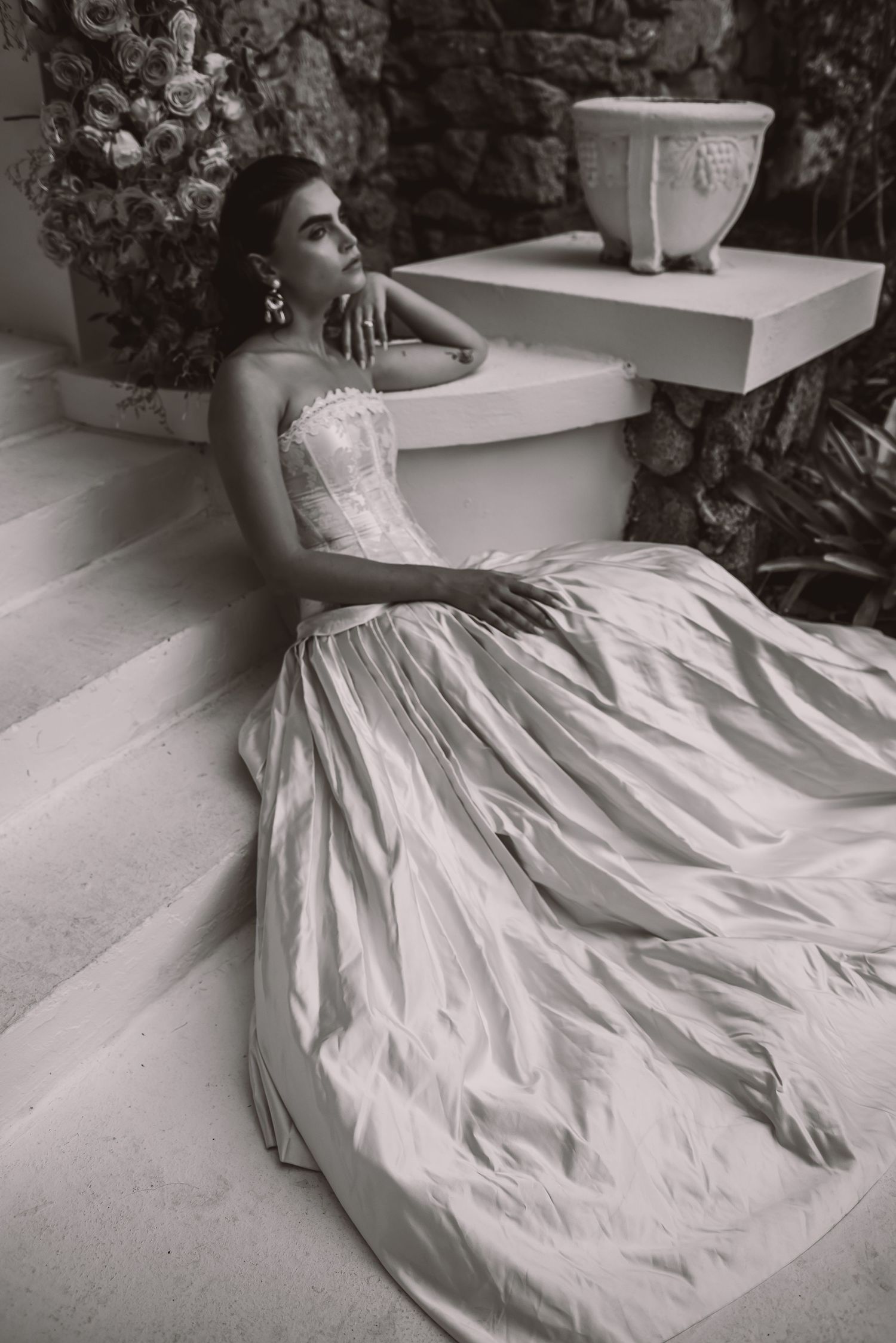 Dramatic black and white bridal portrait with flowing ballgown dress beside decorative vase.