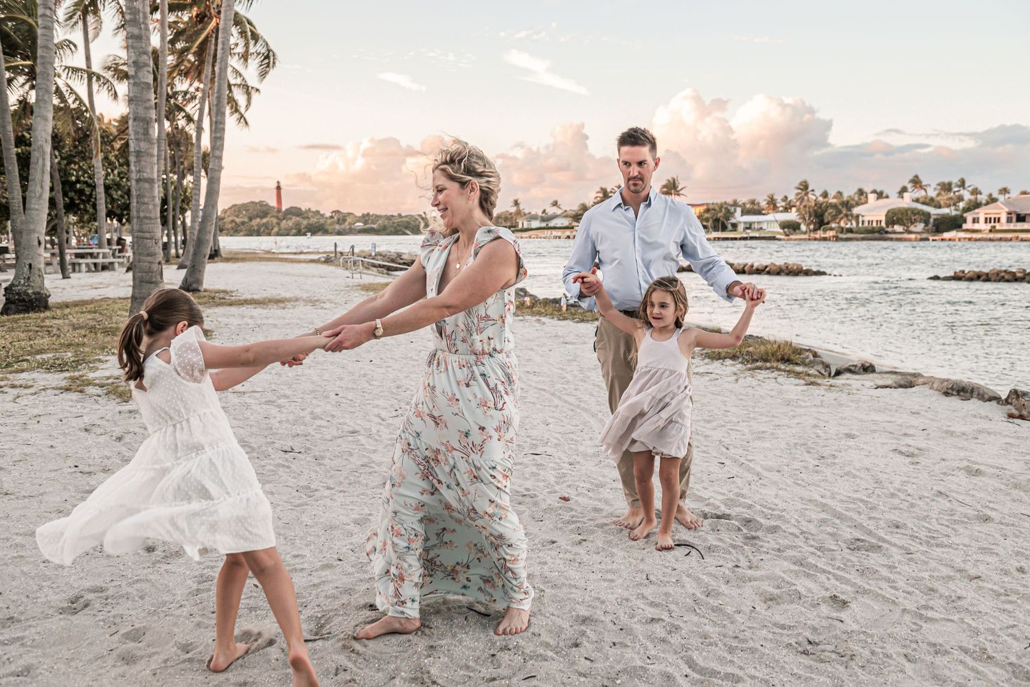 A happy family enjoying a sunset walk together on a tropical beach with palm trees and shoreline in the background.