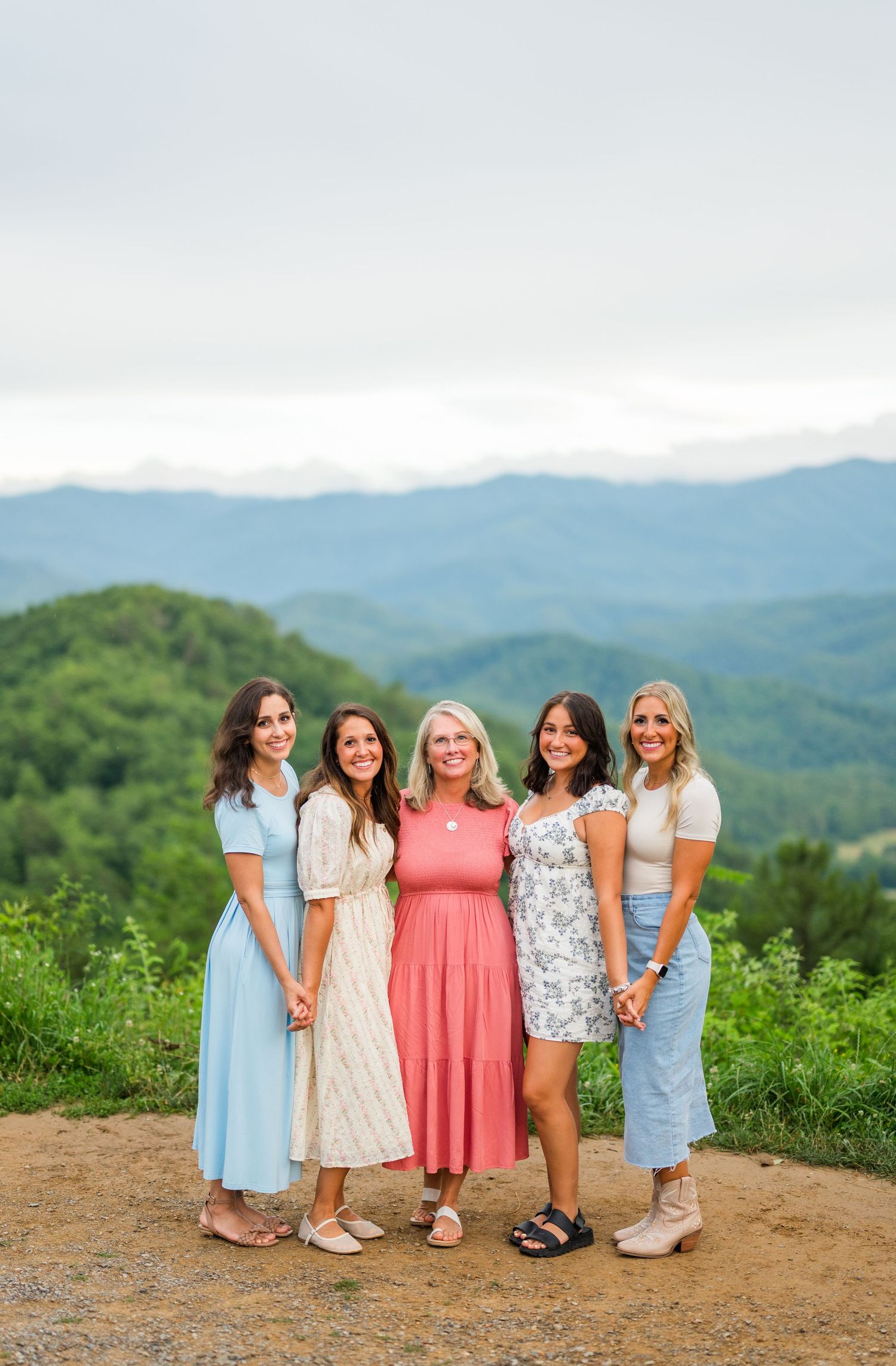 A group of friends in summer dresses pose together with scenic mountain views in the background.