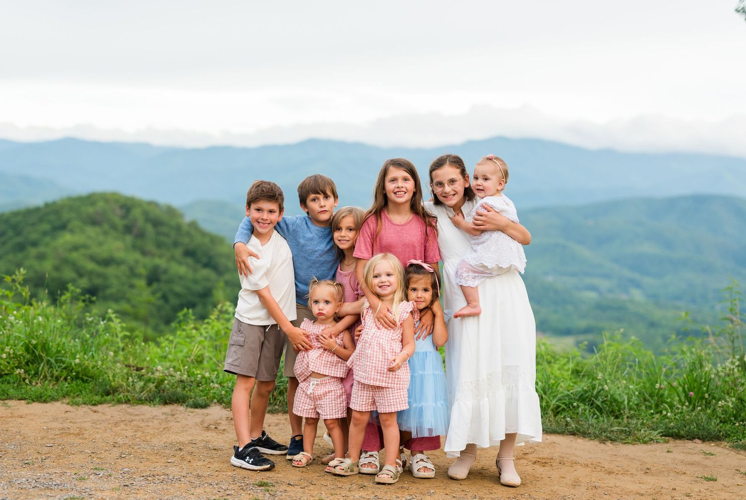A group stands together on a hilltop with rolling green mountains and valleys stretching into the distant background.