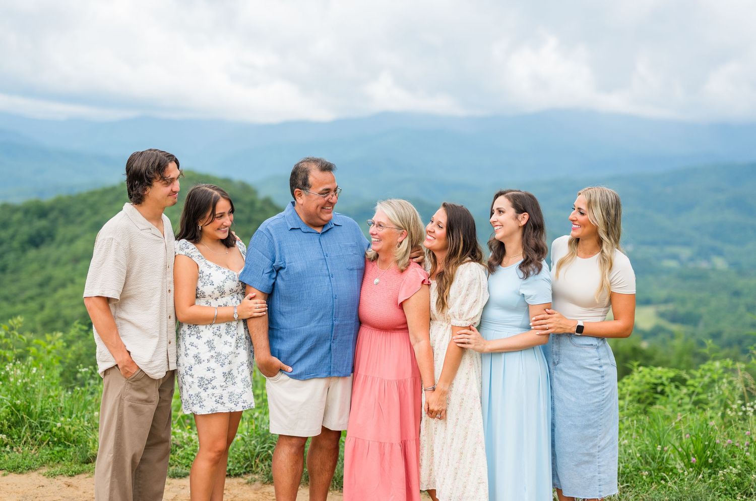 A group in coordinated pastel outfits sharing candid moments during an outdoor mountain photoshoot.