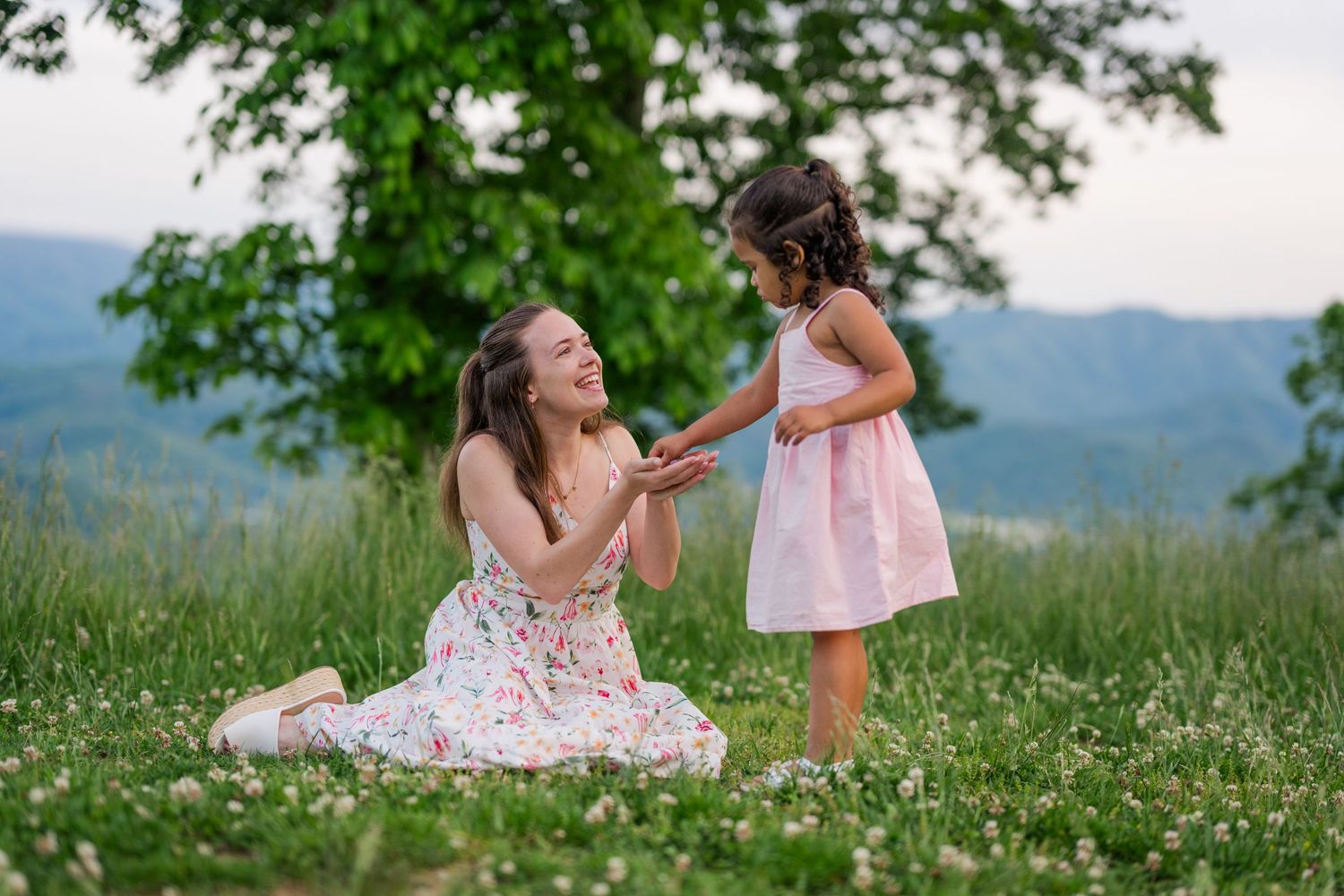 Two people share a tender moment in a flowery meadow with mountains in the background.