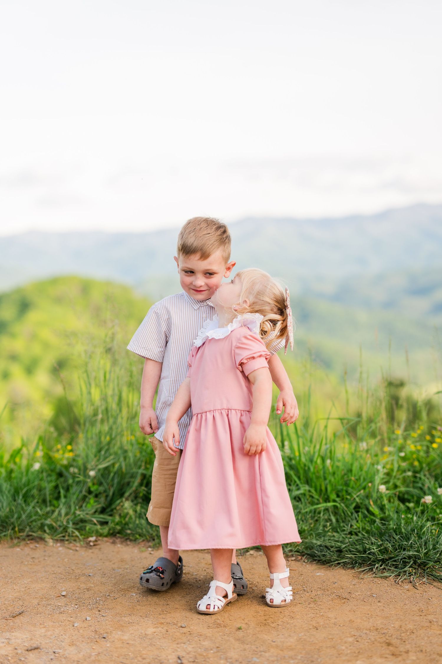Two young children stand together on a dirt path overlooking green mountain scenery on a bright summer day in Pigeon Forge, TN