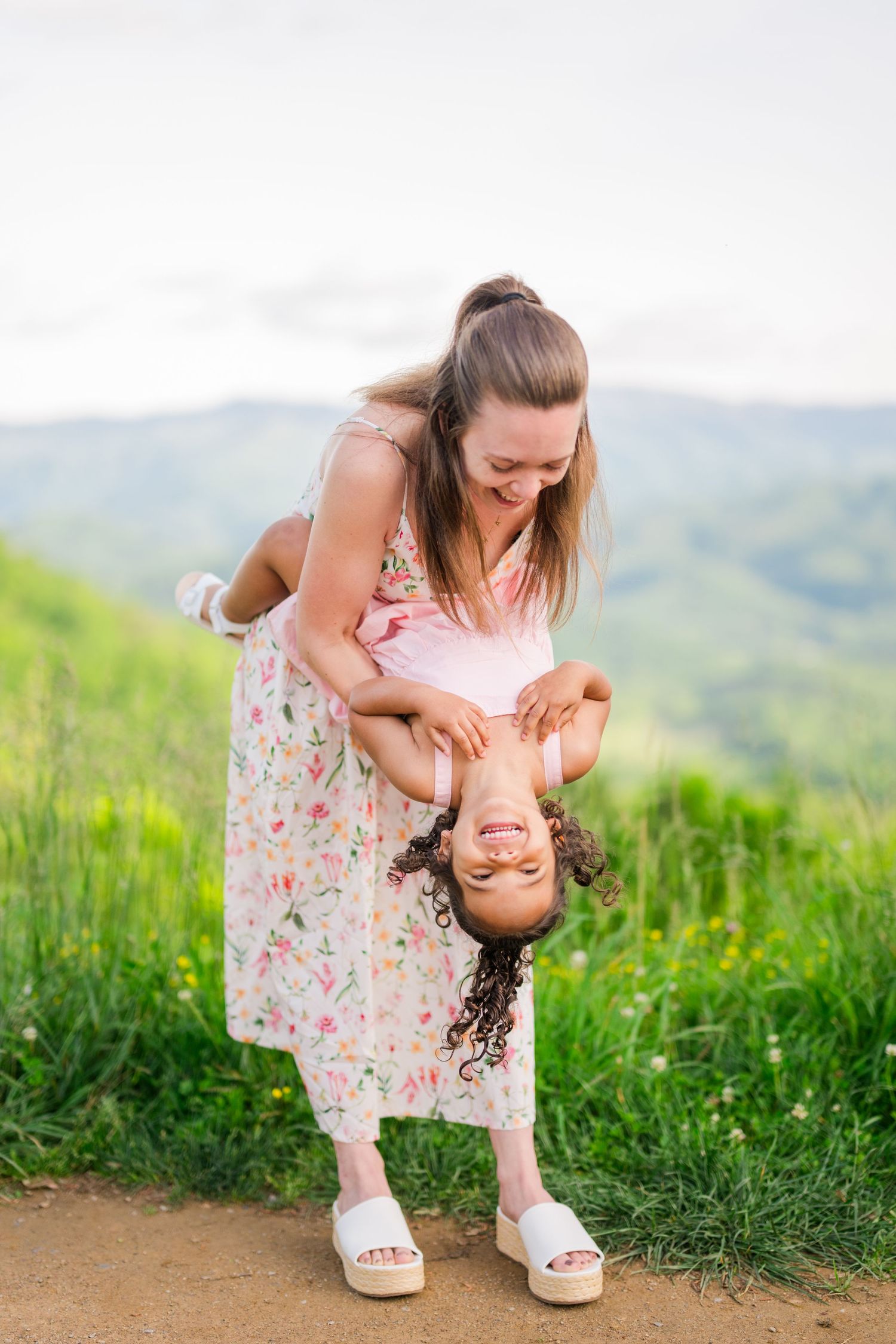 oyful moment shared in a floral dress on a green hillside with mountains in the background between mom and daughter in the Smoky Mountains