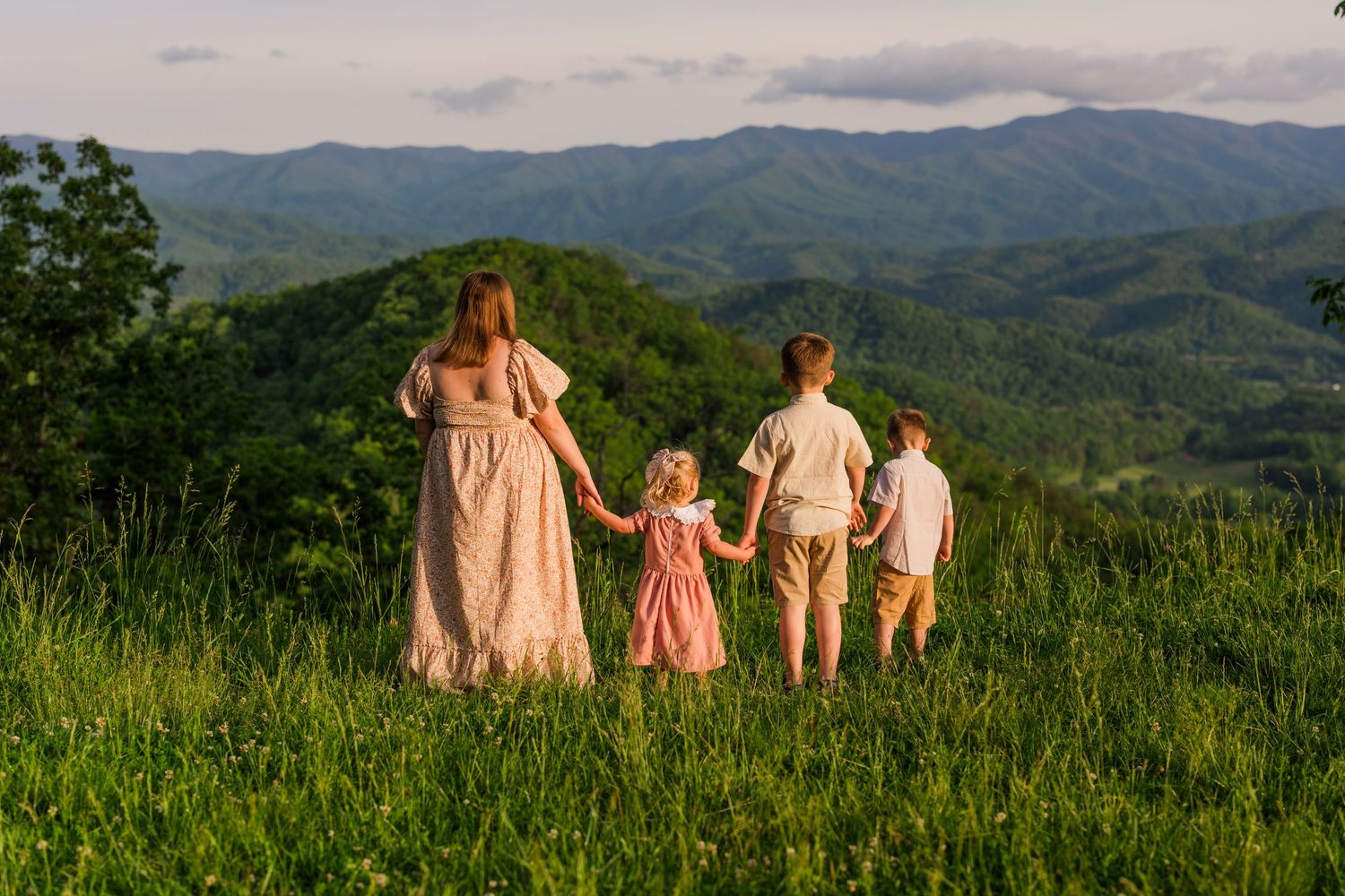 A group stands together on a grassy hilltop overlooking a lush mountain landscape at sunset.