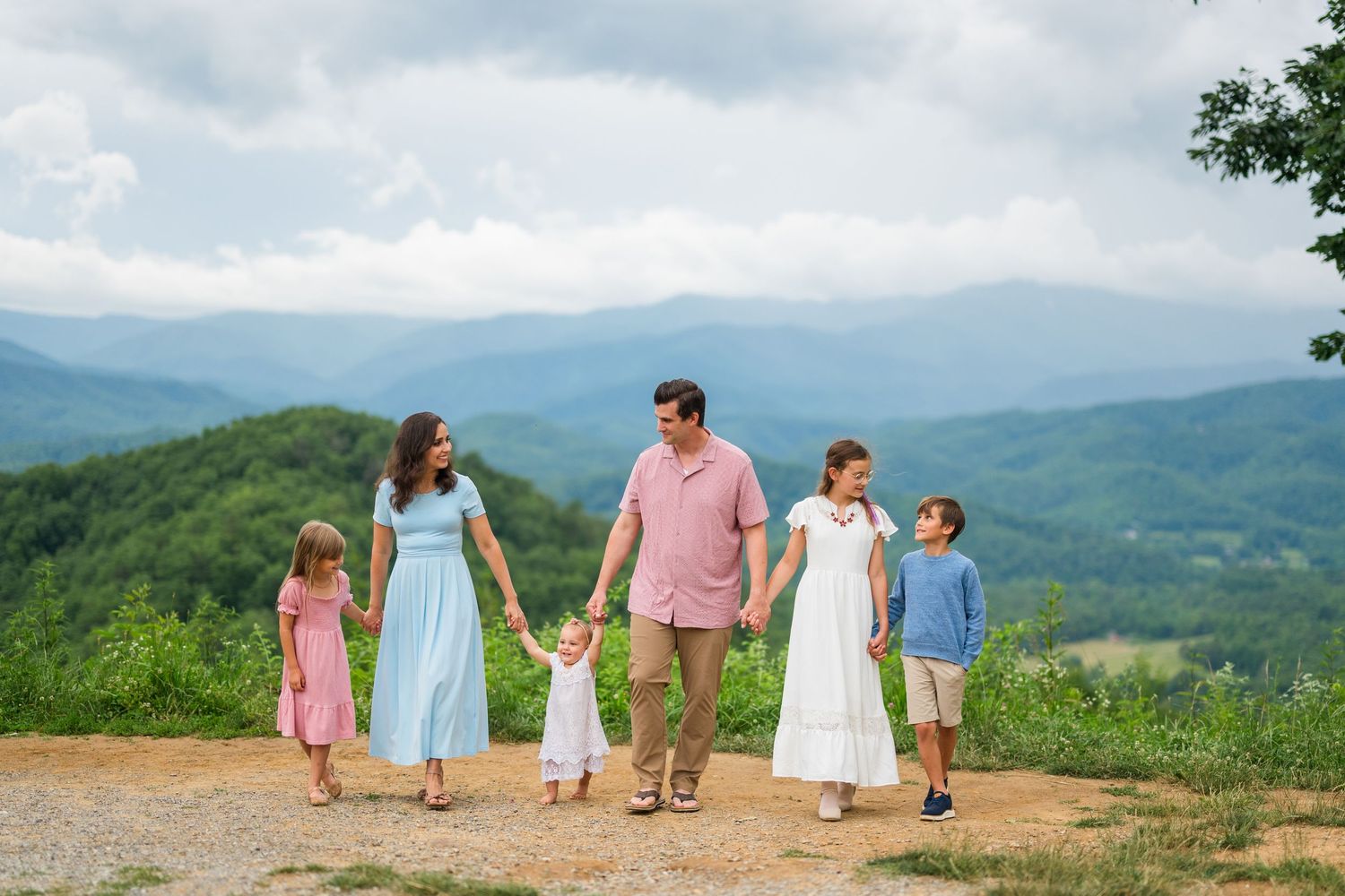 A group of people walk along a scenic mountain ridge enjoying panoramic views of green rolling hills under cloudy skies.