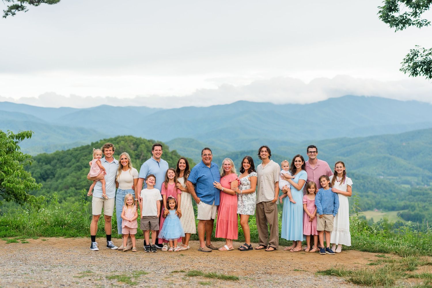 A group stands together on a mountaintop overlook with a scenic view of blue ridge mountains in the background.