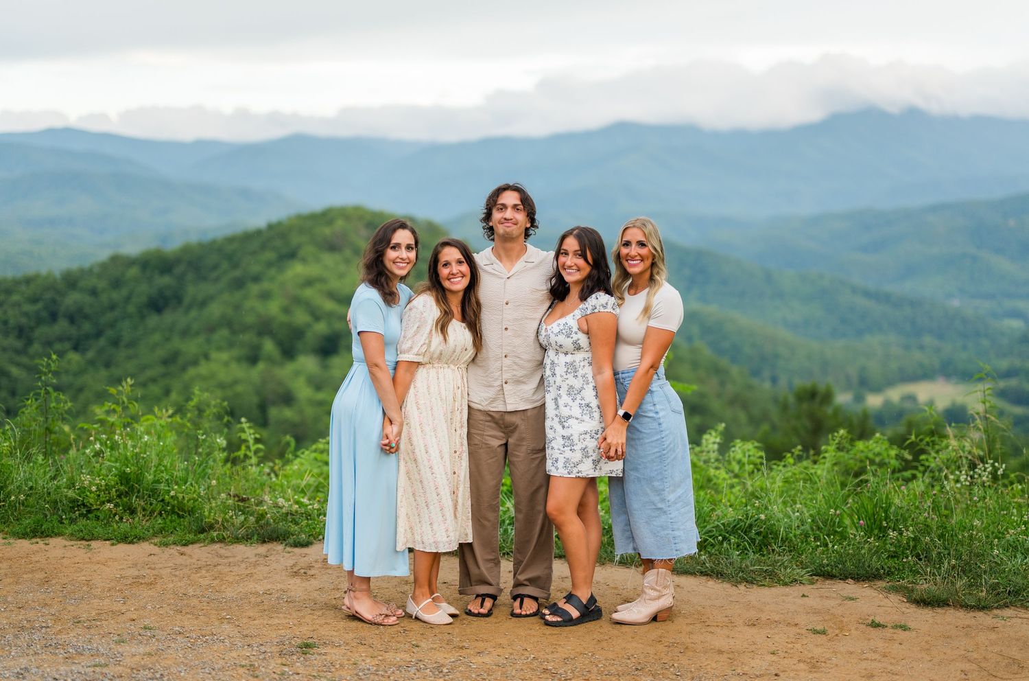 A group poses together on a hilltop overlook with rolling green mountains and misty skies stretching into the distance.