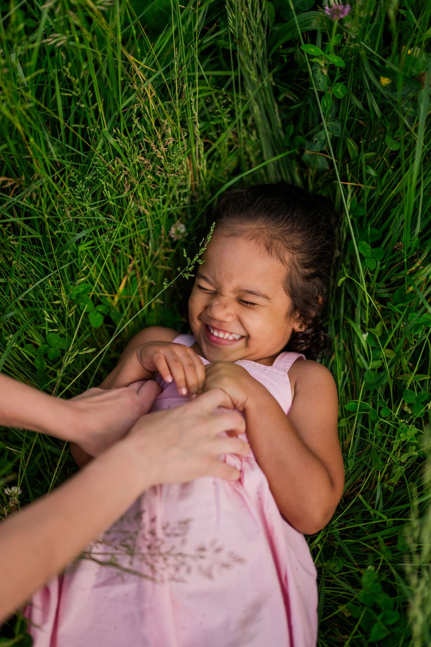 Person playing in tall green grass wearing a pink dress while being tickled and laughing joyfully in the Smoky Mountains