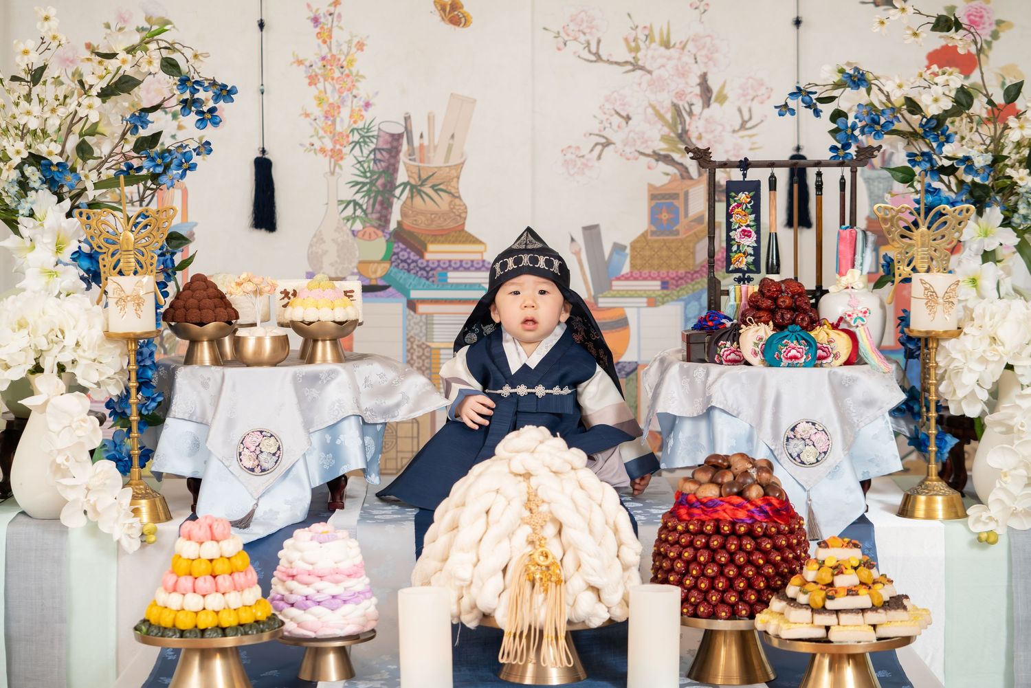 Decorative birthday party setup with multiple cakes and floral arrangements.