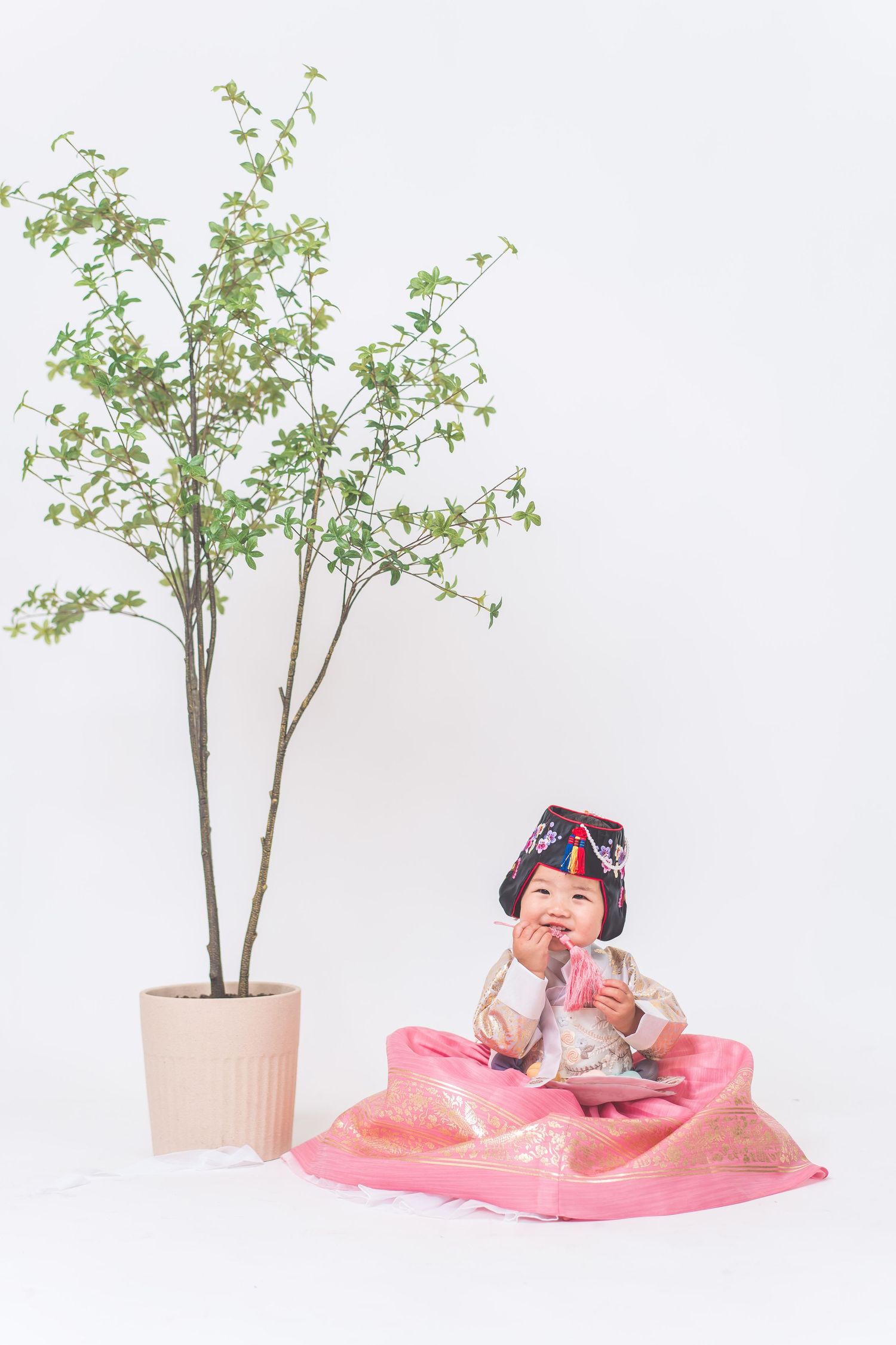 Small doll figure with VR headset sits on pink fabric next to potted plant in minimalist composition.