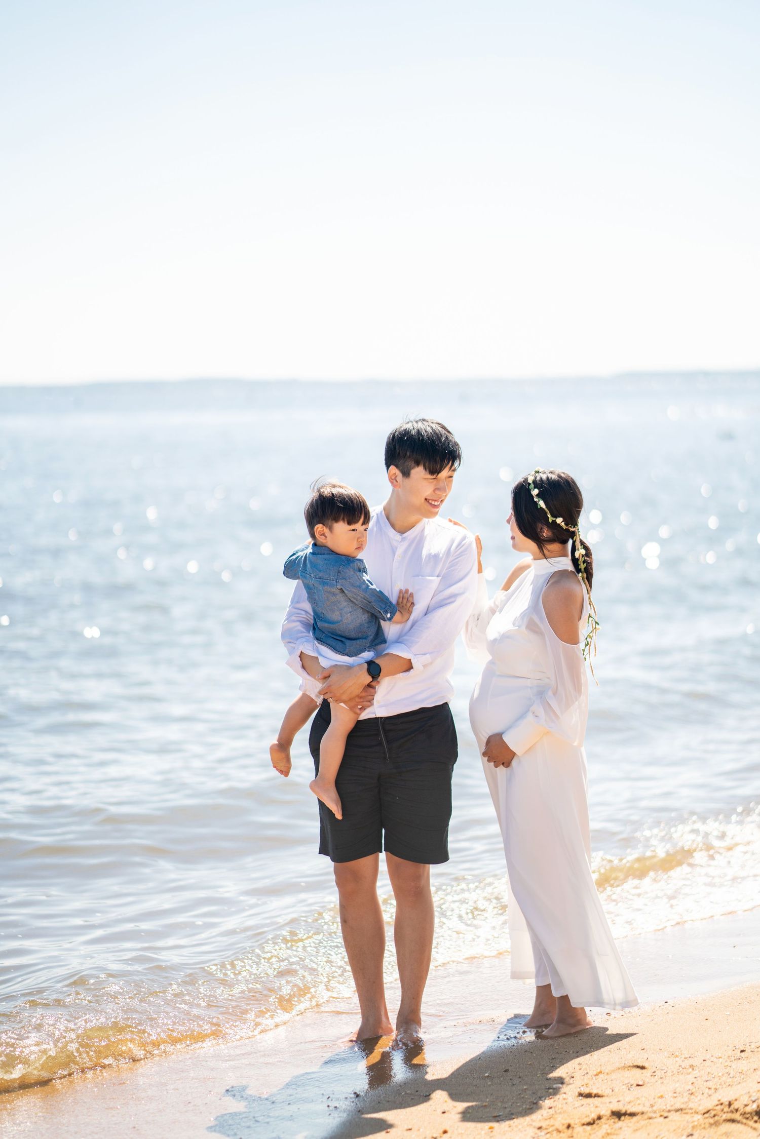 Family enjoying a sunny day together on the beach with ocean waves in background.