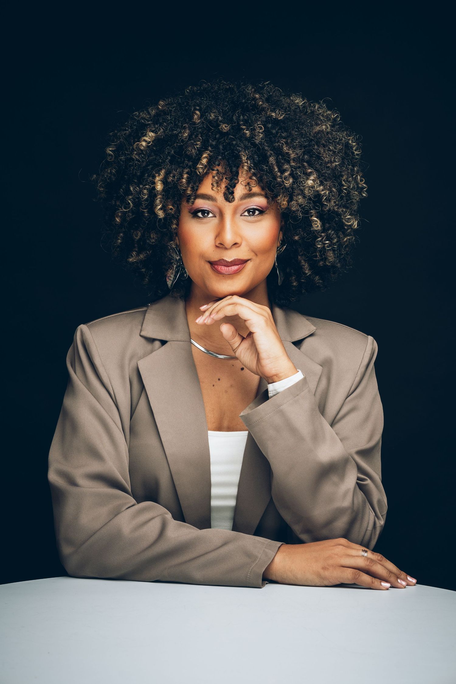 Professional studio portrait featuring a grey blazer and natural curly hair against a dark background.