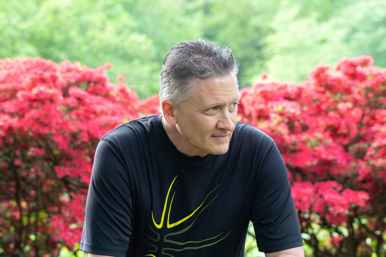 Gray-haired man sitting on a bench in front of azaleas looking away at Sherwood Gardens Baltimore Maryland