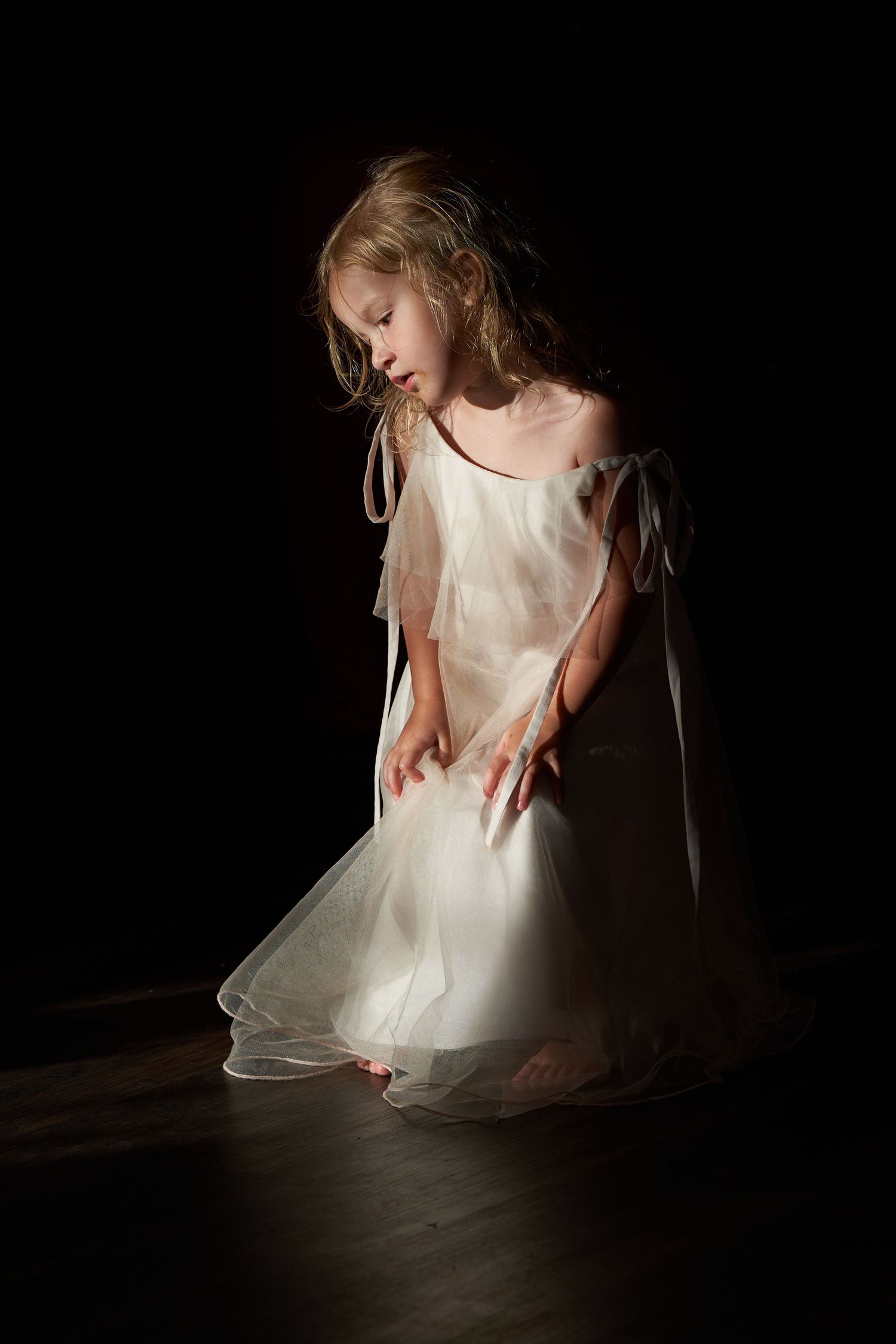 A dancer in a flowing white dress creates a series of graceful movements against a dark background in artistic lighting.