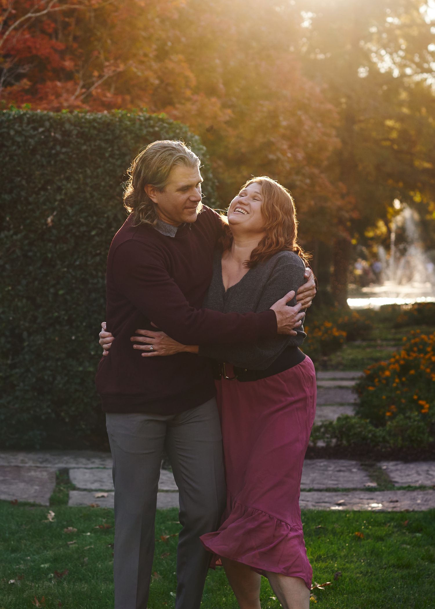 A sweet couple embraces and shares a joyful laugh together at sunset in a garden with autumn foliage.