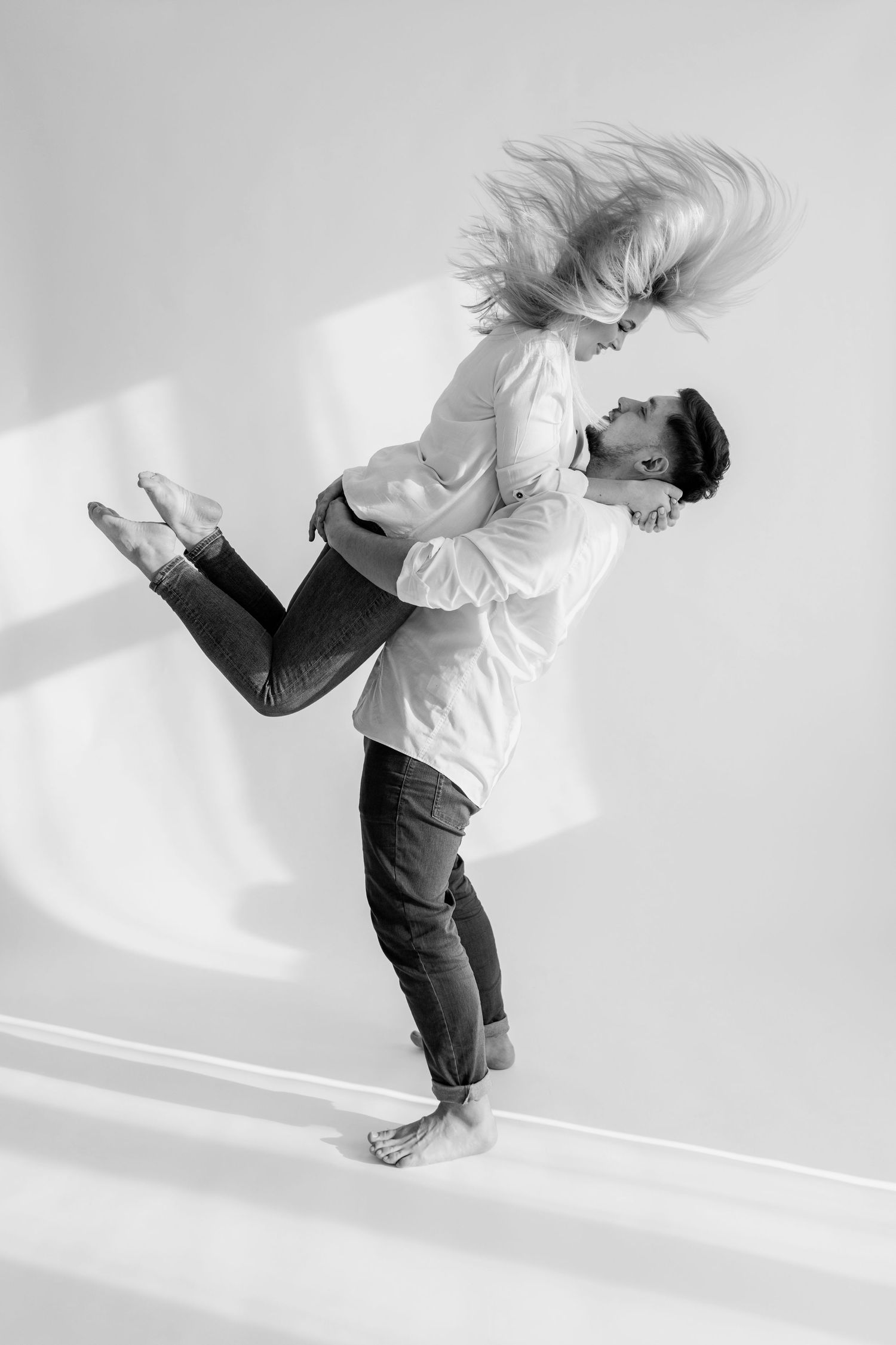 Dynamic black and white photo of couple in dramatic lifting pose against white wall.