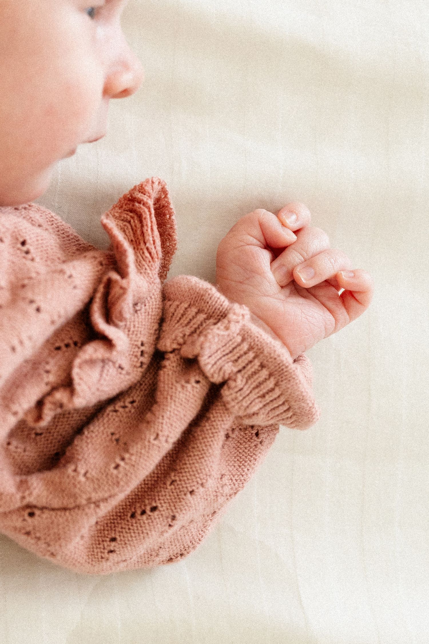 Small hand in a soft dusty pink knitted sweater sleeve on white fabric background.