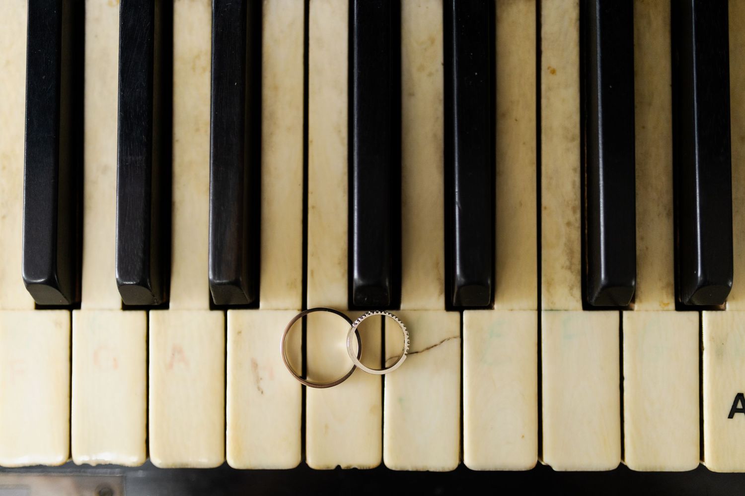 Wedding rings placed on vintage piano keys in soft natural light.