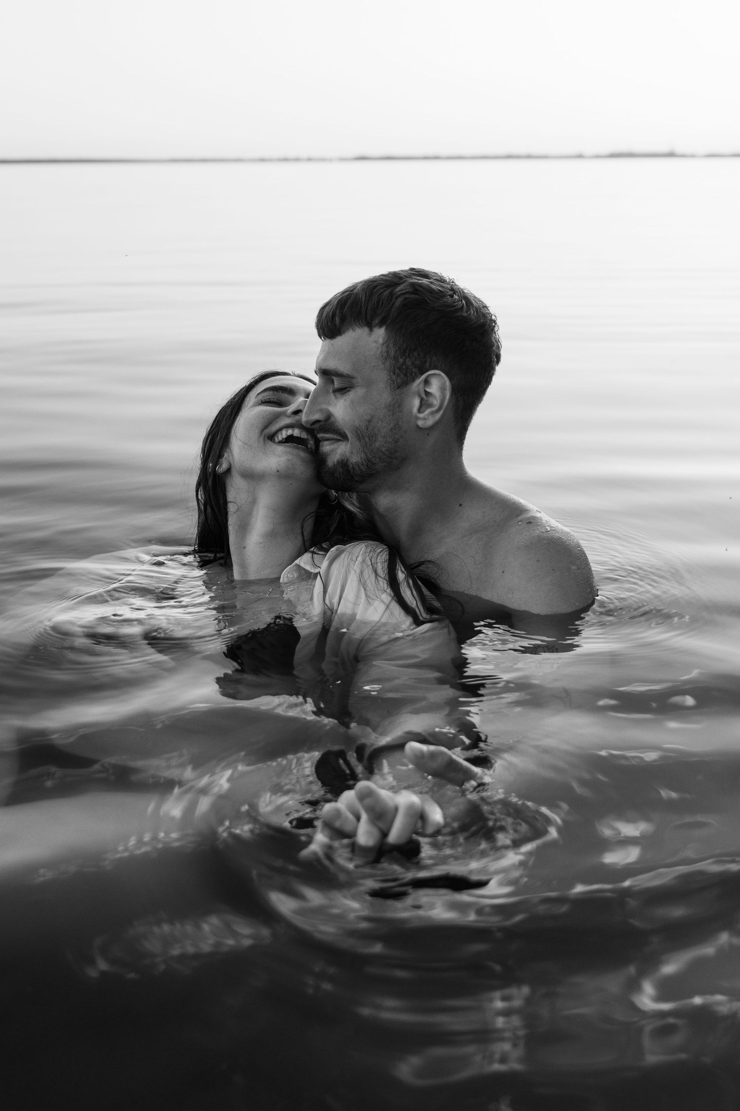 Intimate moment between couple swimming in calm waters at dusk.