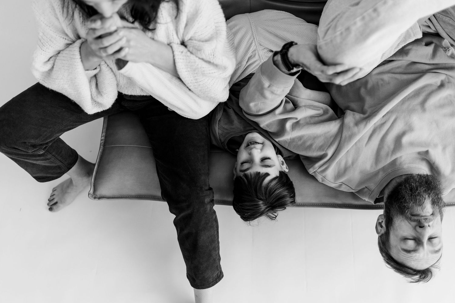 Playful black and white overhead portrait of family lying on floor together.