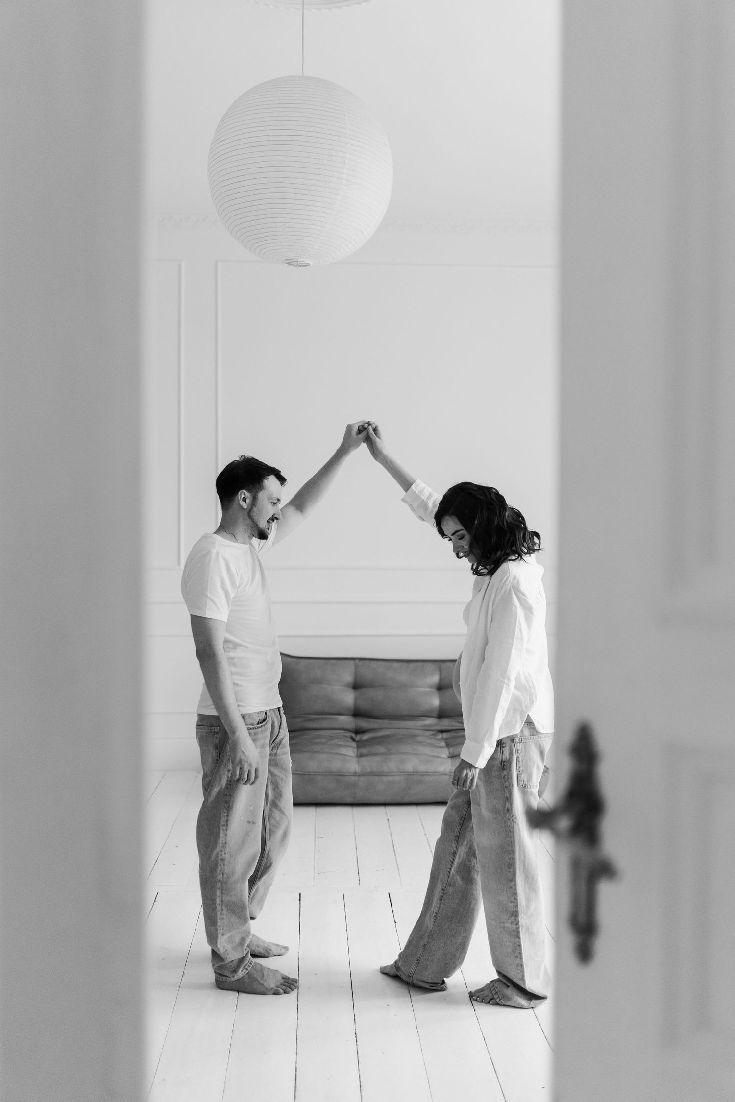 Black and white photo of couple making house shape with raised arms in minimalist setting.