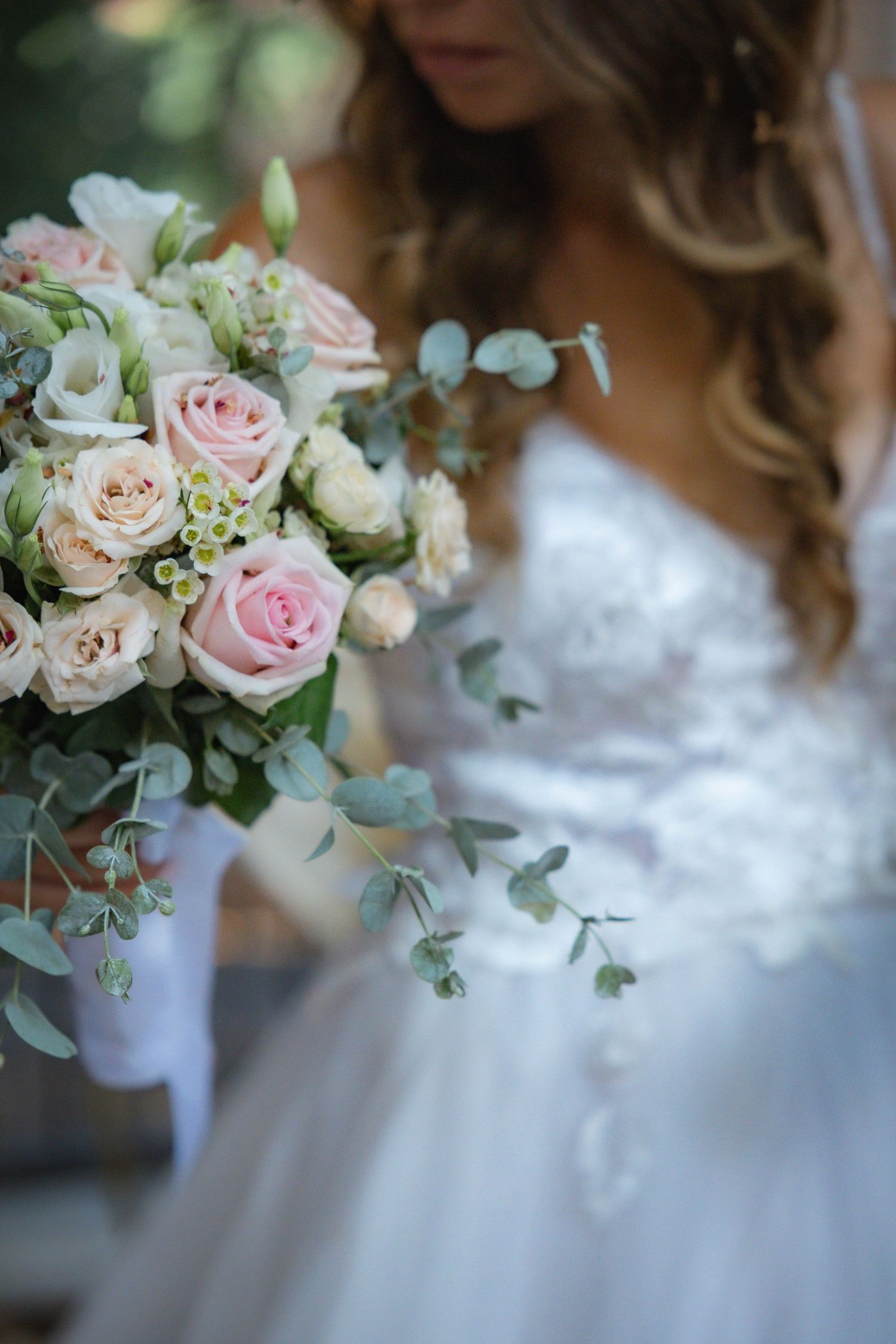 Delicate pink and white roses with eucalyptus leaves in a bridal bouquet against white lace.