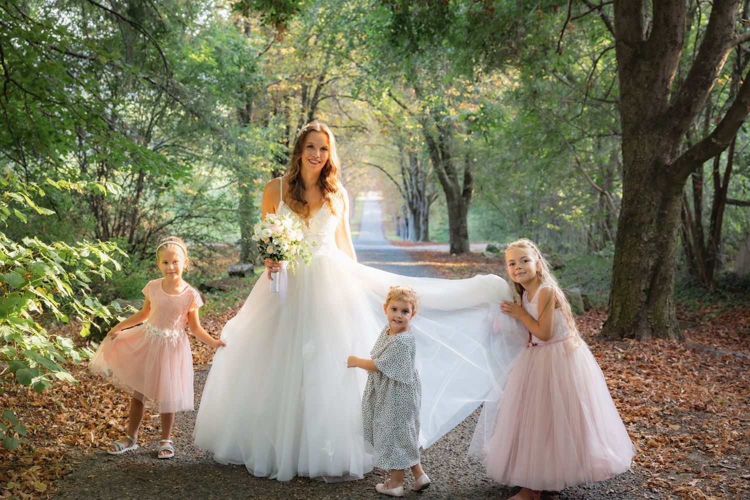 Wedding party in white and blush dresses poses for photos in a scenic wooded area.