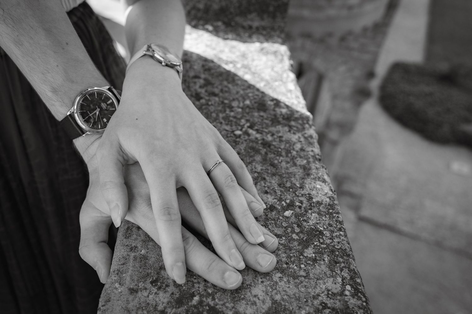 Black and white close-up of hands gently touching on a stone surface.