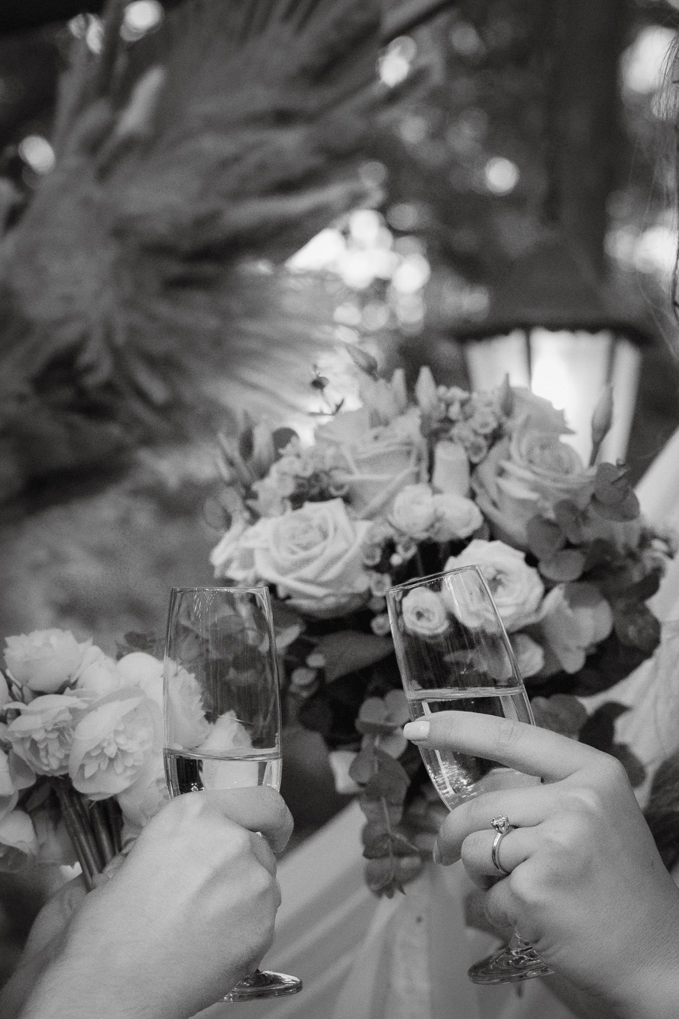 Champagne glasses clink in celebration with elegant roses in a black and white wedding photo.