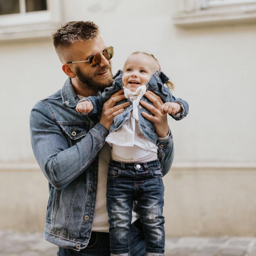 Father in denim jacket sharing joyful moment with young child outdoors.