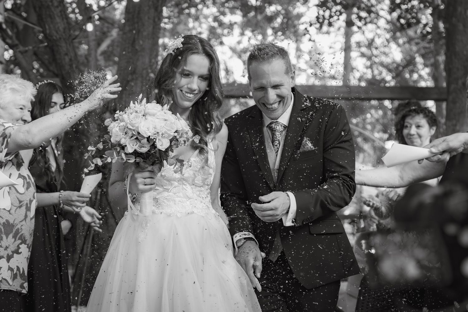 Candid black and white wedding photo capturing couple's genuine laughter in an outdoor setting.