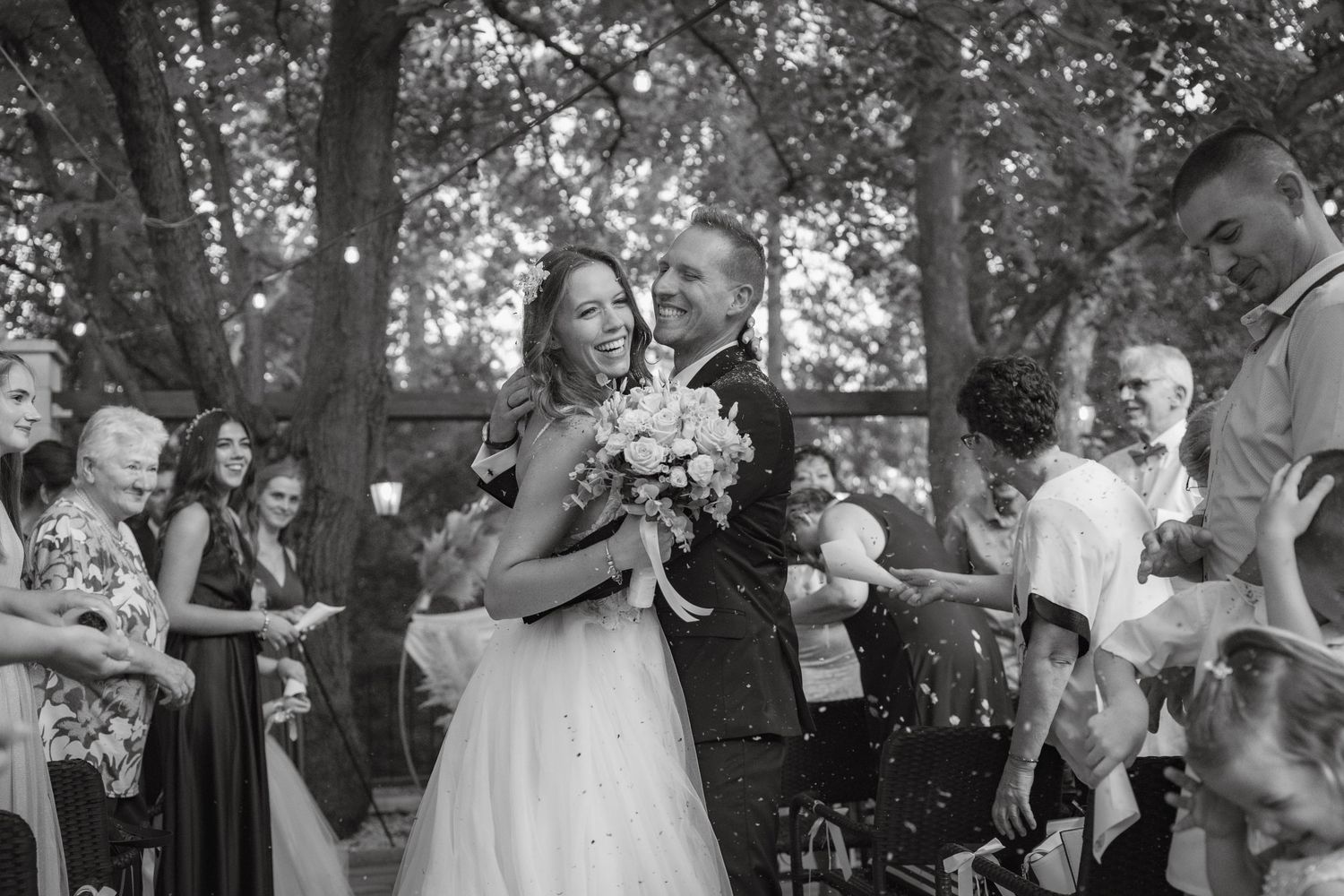 Candid black and white shot of bride and groom sharing happy moment during outdoor ceremony.