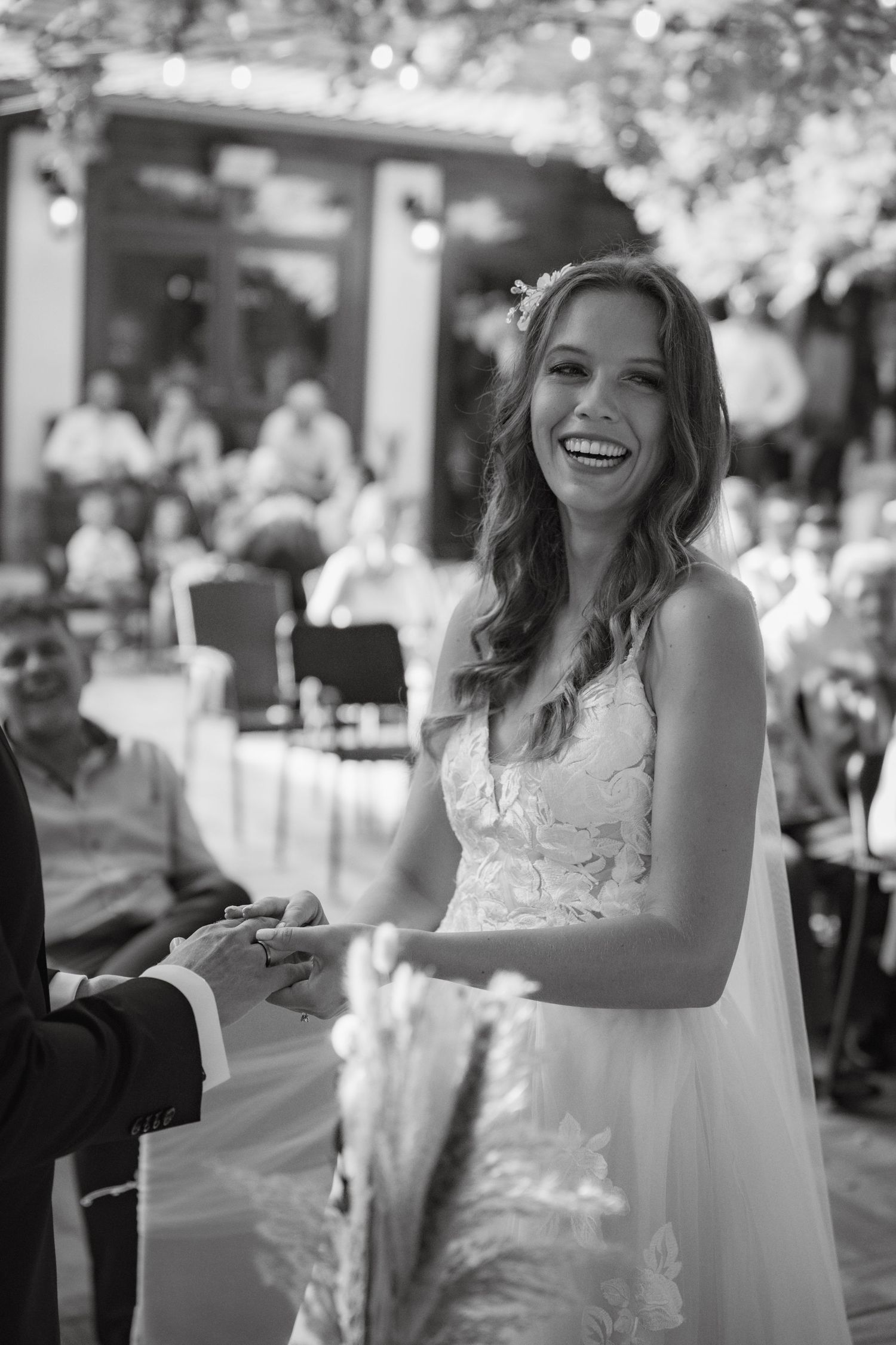 A bride in a white lace dress laughs joyfully during her outdoor wedding celebration.