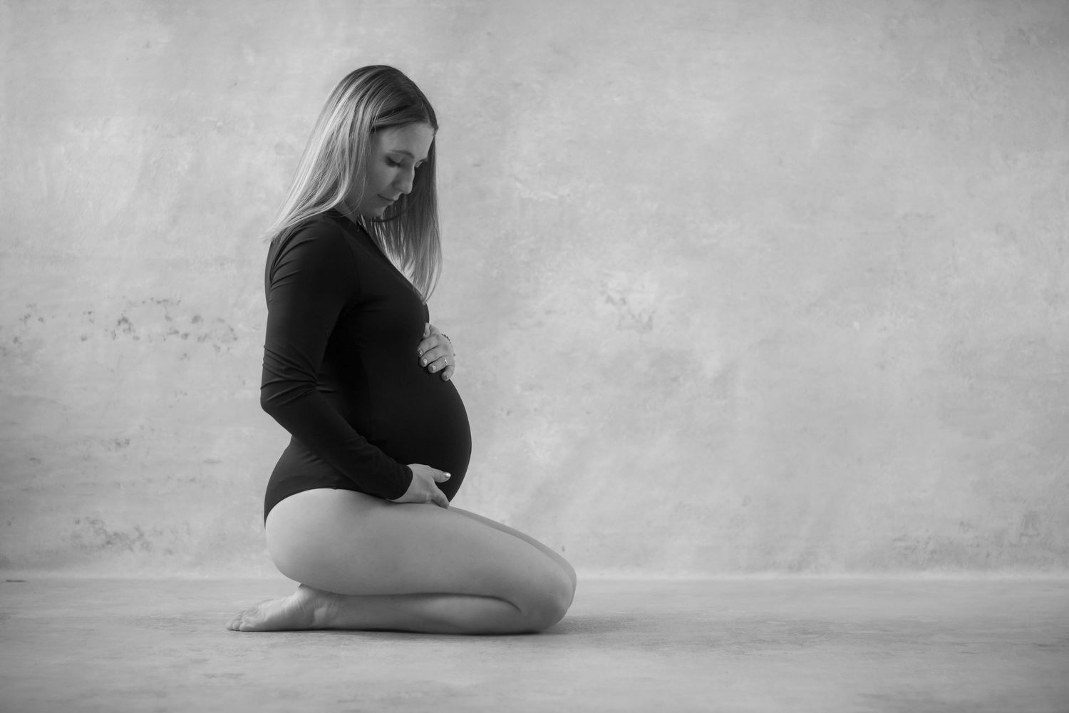 An artistic black and white maternity photo showing a woman in a minimalist setting.