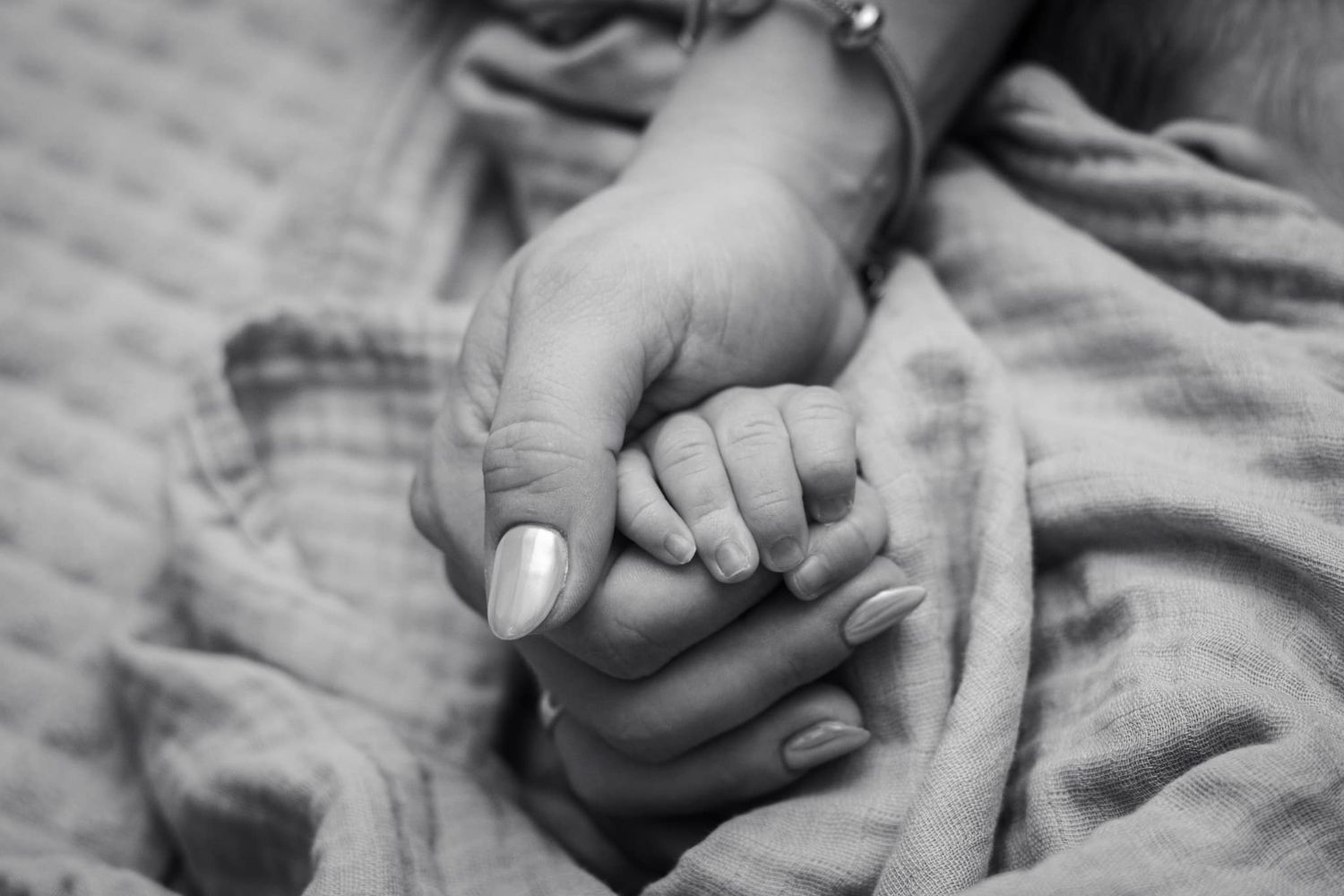 Close-up detail of gentle hands holding tiny baby fingers against textured fabric.