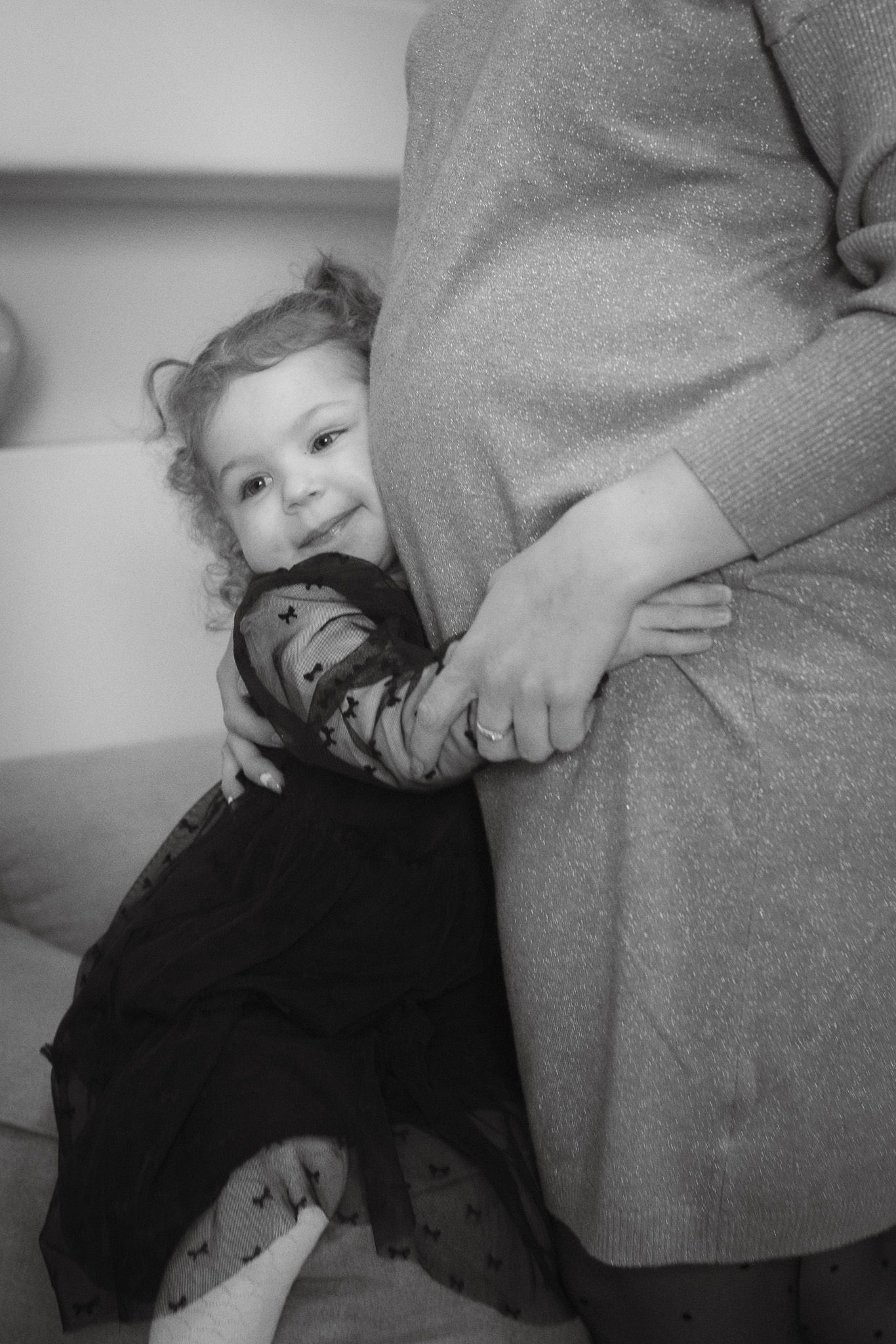 Black and white candid moment of young child hugging expectant mother.