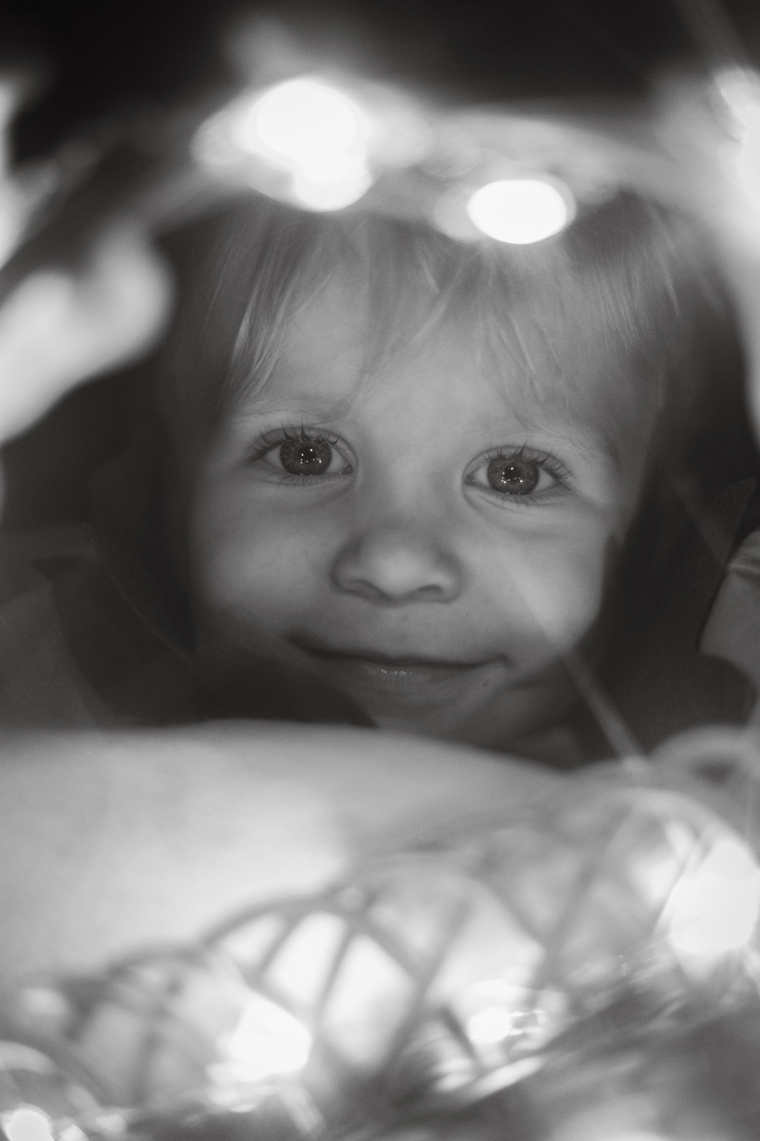 Close-up black and white portrait of eyes peeking through soft bokeh lights.