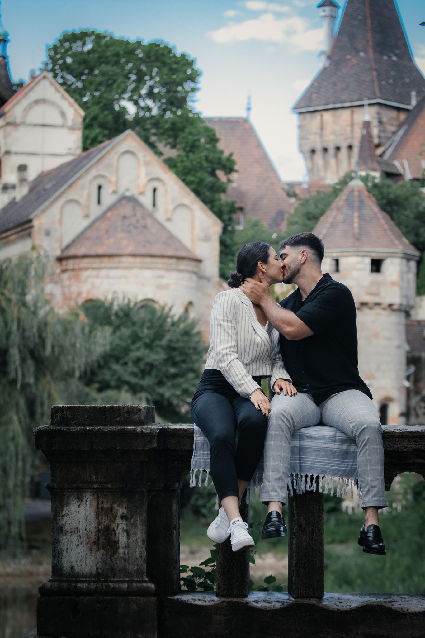 Couple sharing intimate moments on stone wall with historic church architecture in background.