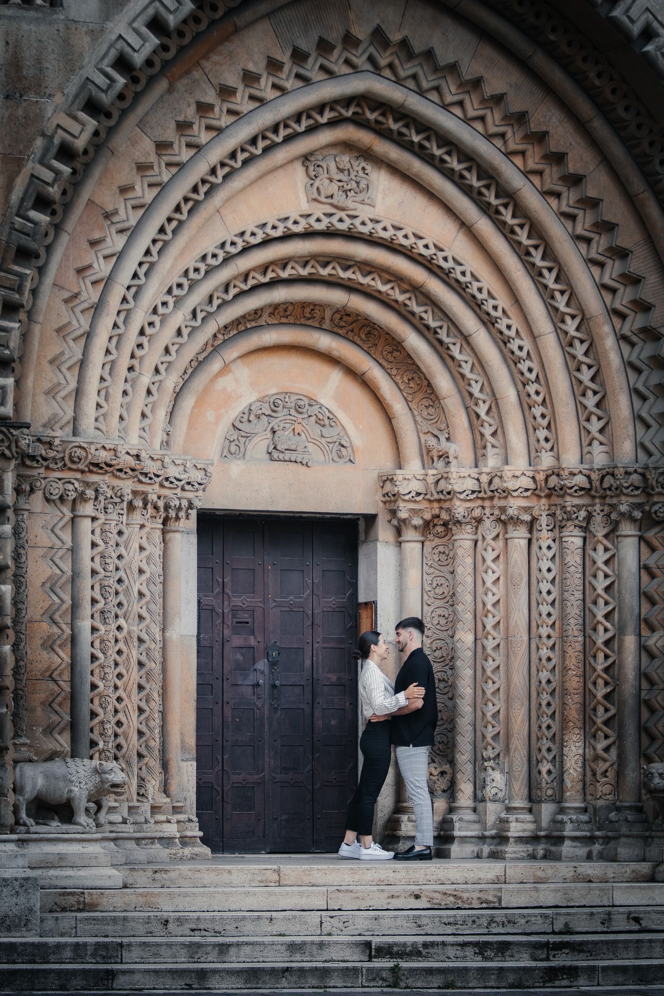 Couple embracing at ornate medieval church entrance with intricate stone archway details.