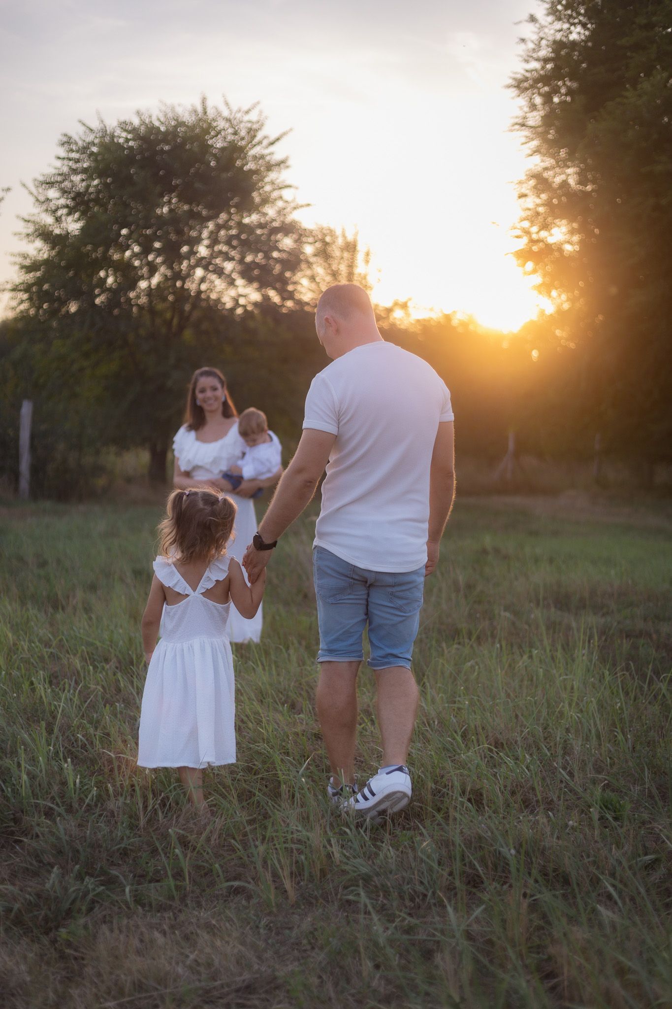 Family walking together in a field at sunset with golden light filtering through trees.