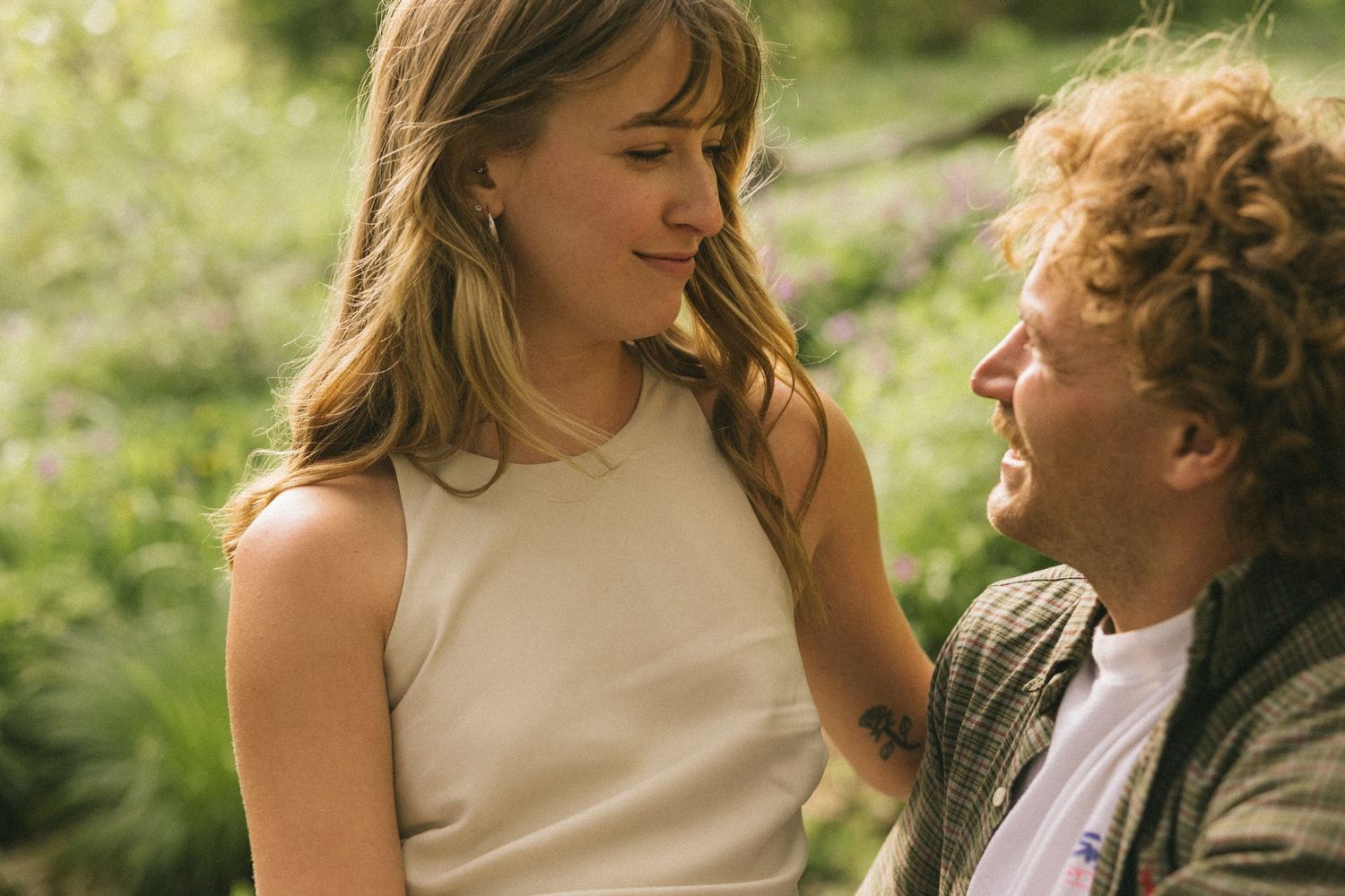 A romantic couple embraces outdoors in a garden setting during a sunny afternoon shoot in nature.
