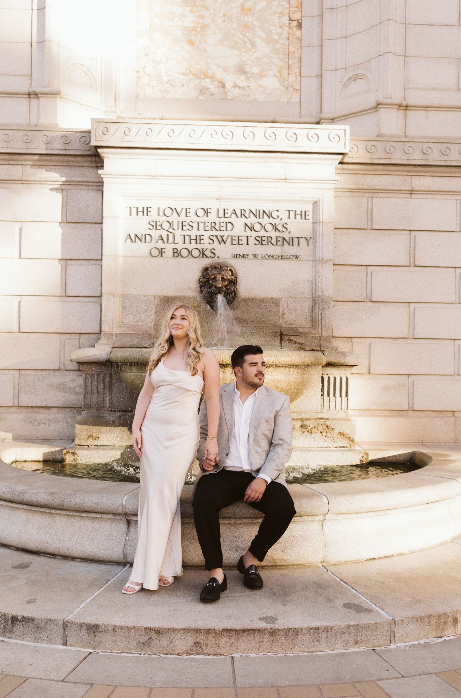 Couple posing by a decorative stone fountain with carved text.