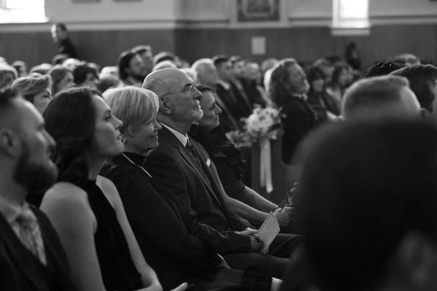 A crowd of formally dressed guests seated in church pews during a wedding ceremony.