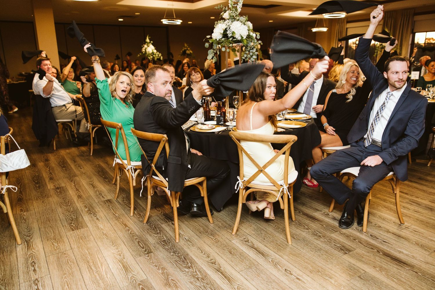 Wide view of wedding reception venue with guests seated at tables on wooden floors.