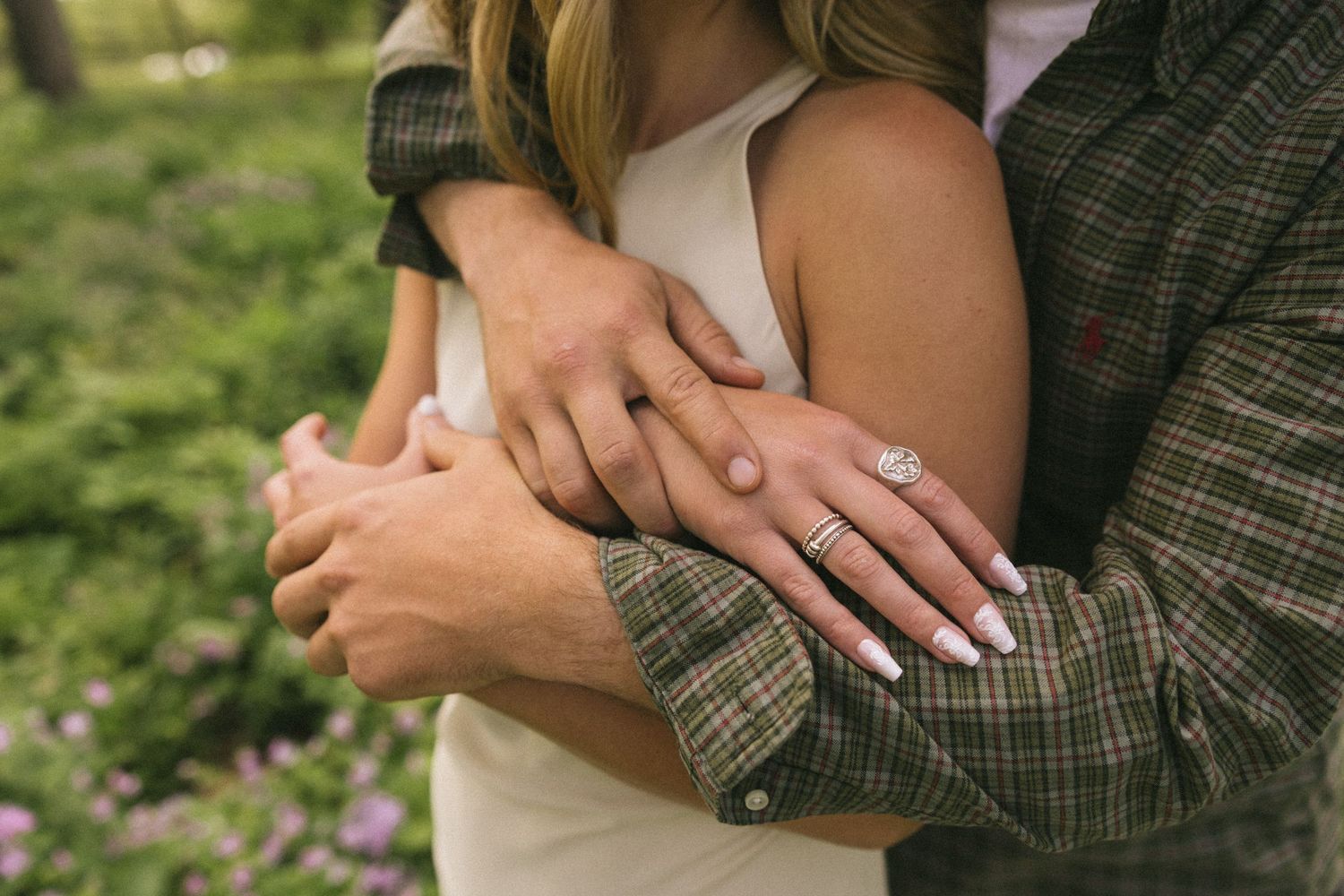 Close-up of hands embracing, showing an engagement ring while wearing plaid and white clothing.